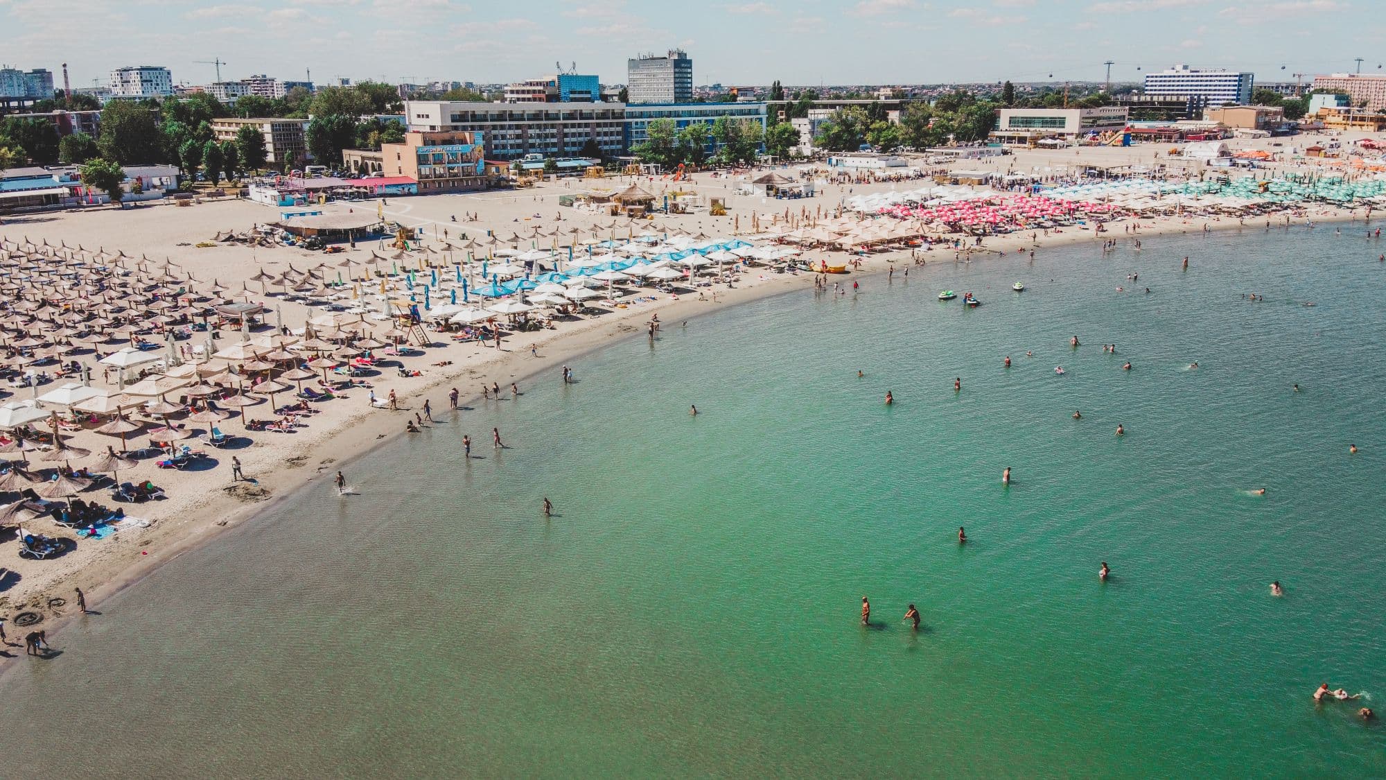 Vedere aeriană a plajei din Georgia cu turiști, șezlonguri colorate, apă turcoaz și clădiri moderne pe malul apei