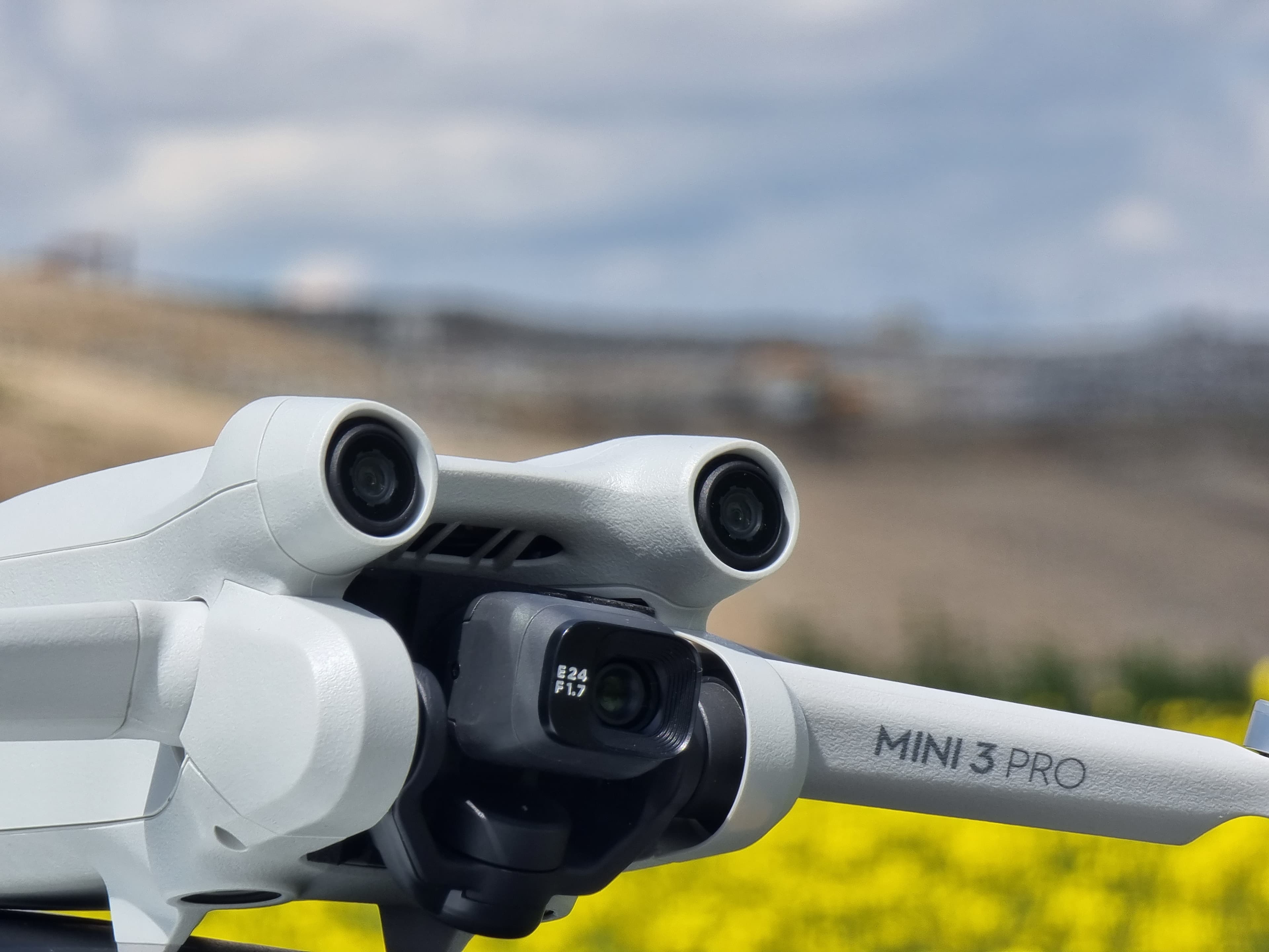 Dronă DJI Mini 3 Pro cu camerele de navigație vizibile, pe fundal cu câmp înflorit