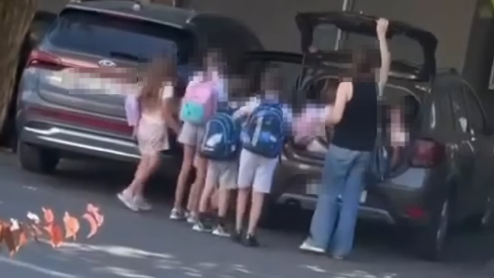 Copii cu ghiozdane urcă în portbagajul deschis al unui autoturism, supravegheați de o femeie; fețele și numerele de înmatriculare sunt acoperite