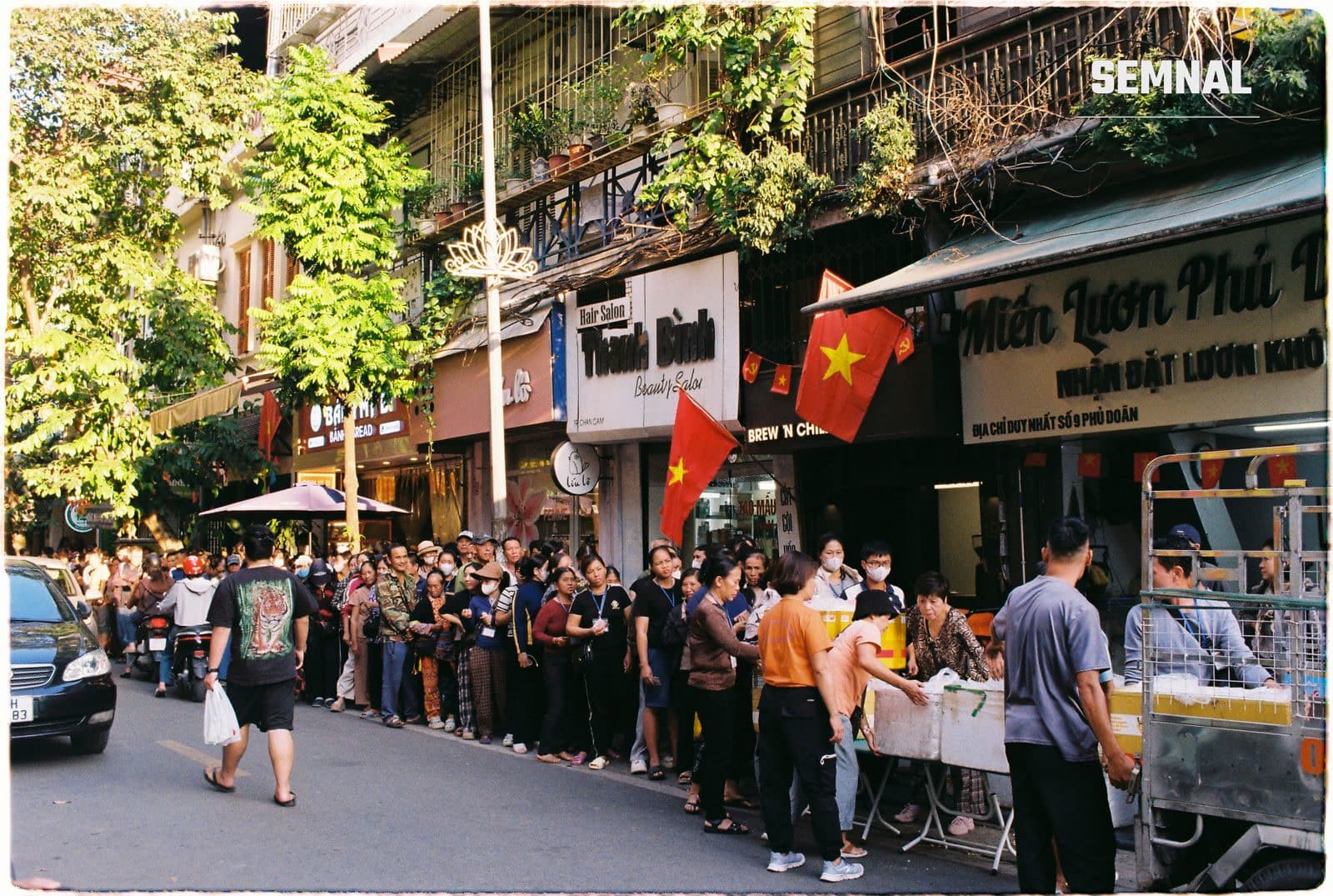 Stradă aglomerată din Hanoi, cu oameni și magazine, ilustrând viața de zi cu zi în Vietnam