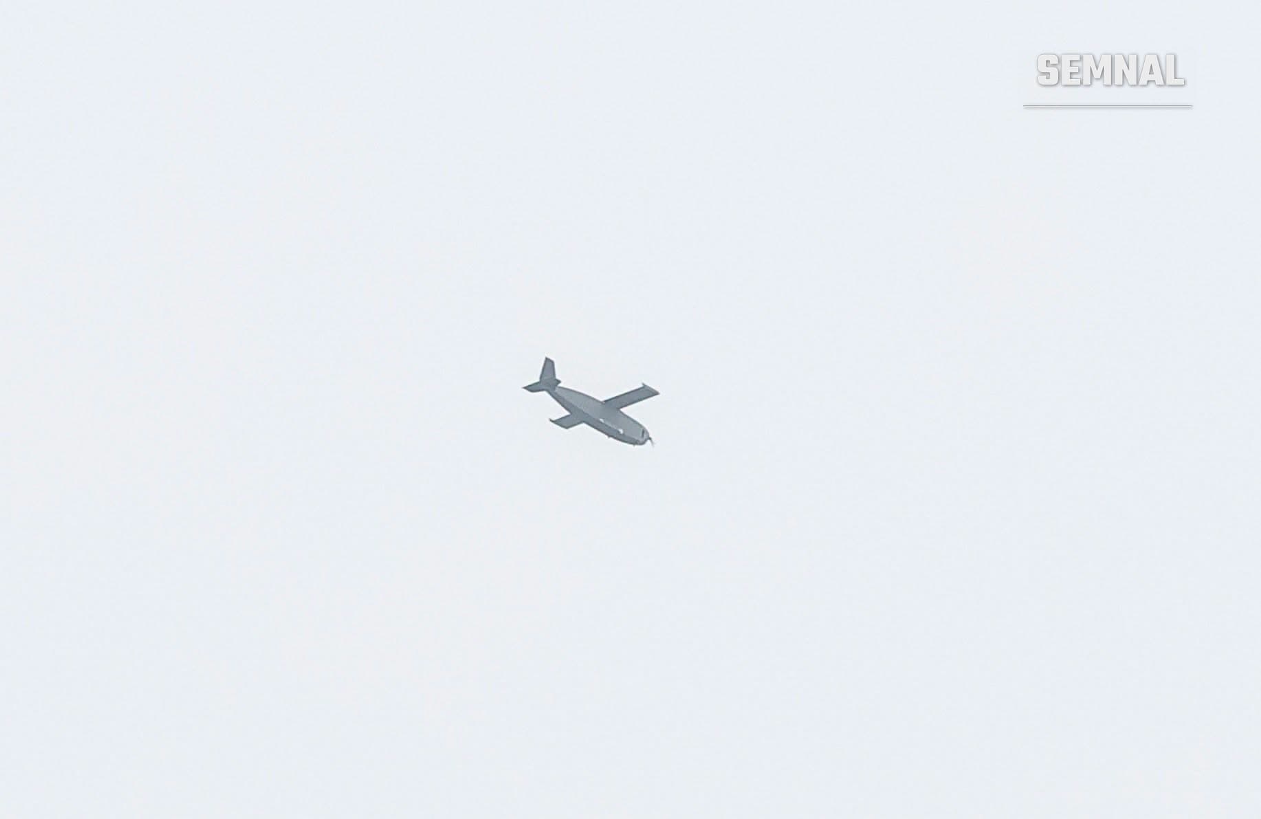 Reprezentare digitală a unei drone cu aripi fixe, gri-închis, în zbor pe fundal gri deschis, ilustrând vehiculul aerian menționat în articolul despre căderea la Plaurul, județul Tulcea.