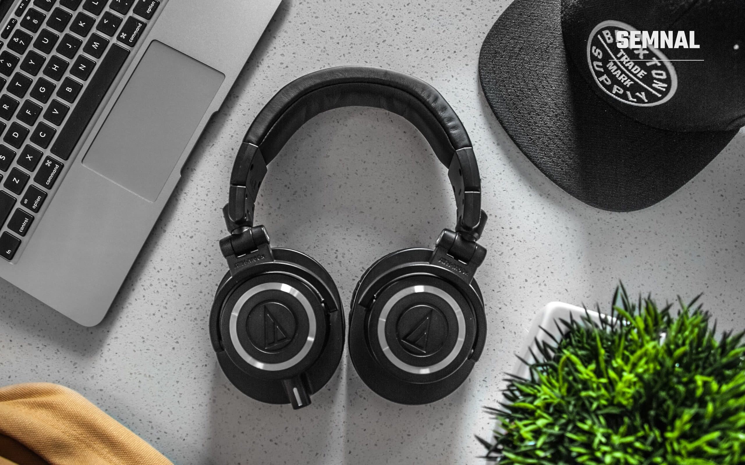 Căști audio negre wireless așezate pe un birou alb, lângă un laptop deschis