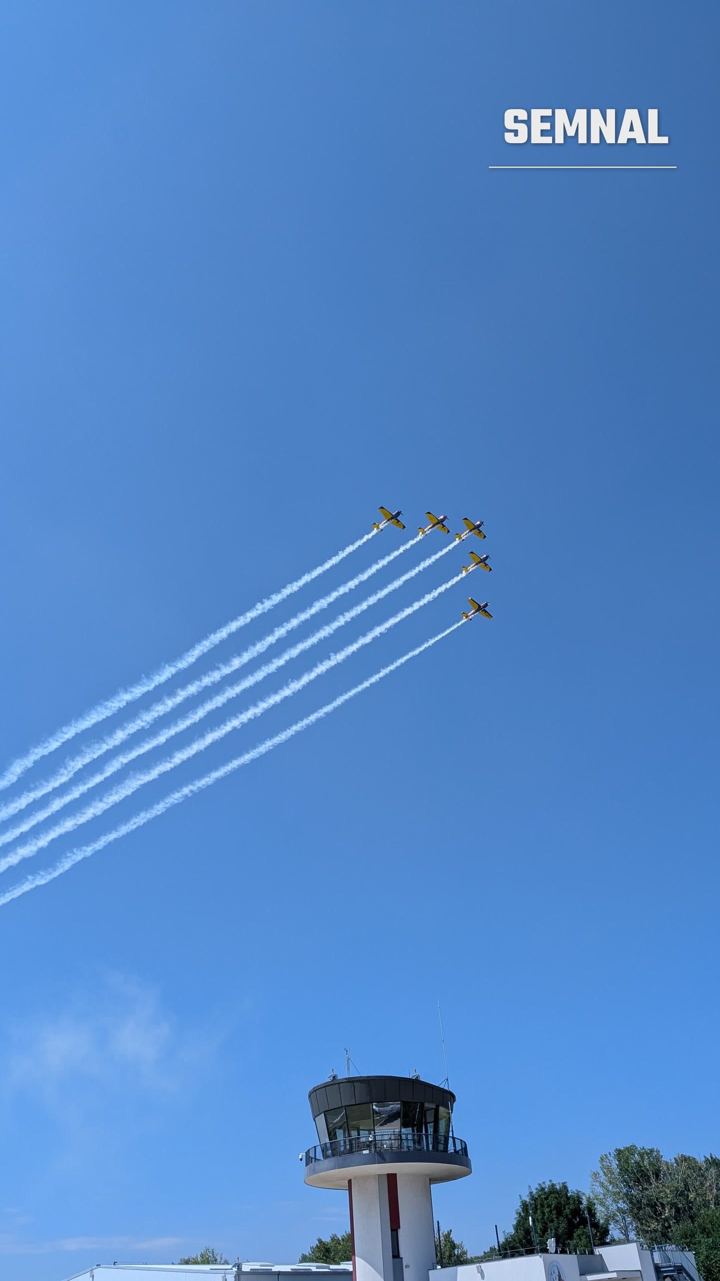 Formație de avioane de acrobație ale Aeroclubului României, cu dâre de fum, deasupra turnului de control de la Clinceni