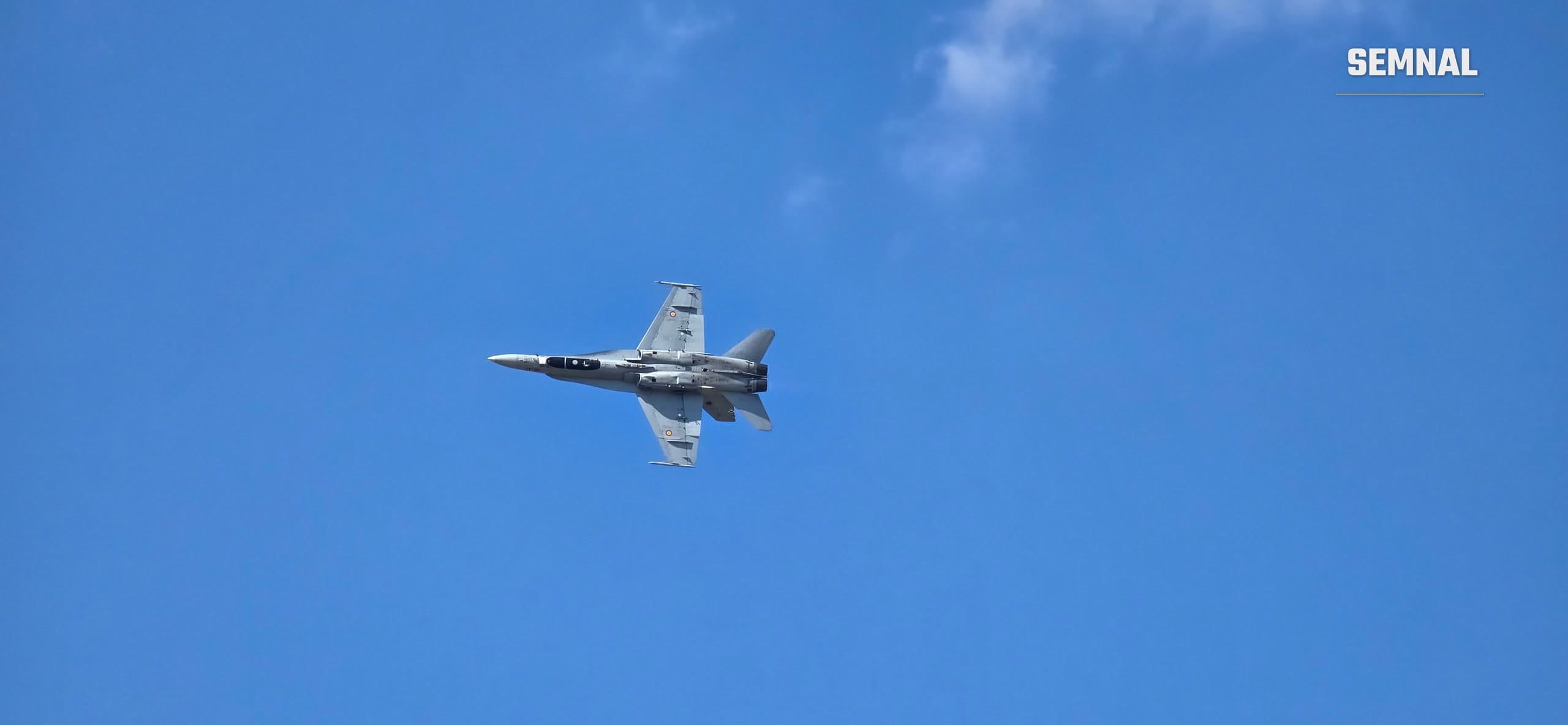 Avion de vânătoare F-18 al Forțelor Aeriene și Spațiale Spaniole în zbor, văzut de dedesubt pe cer senin (imagine ilustrativă)