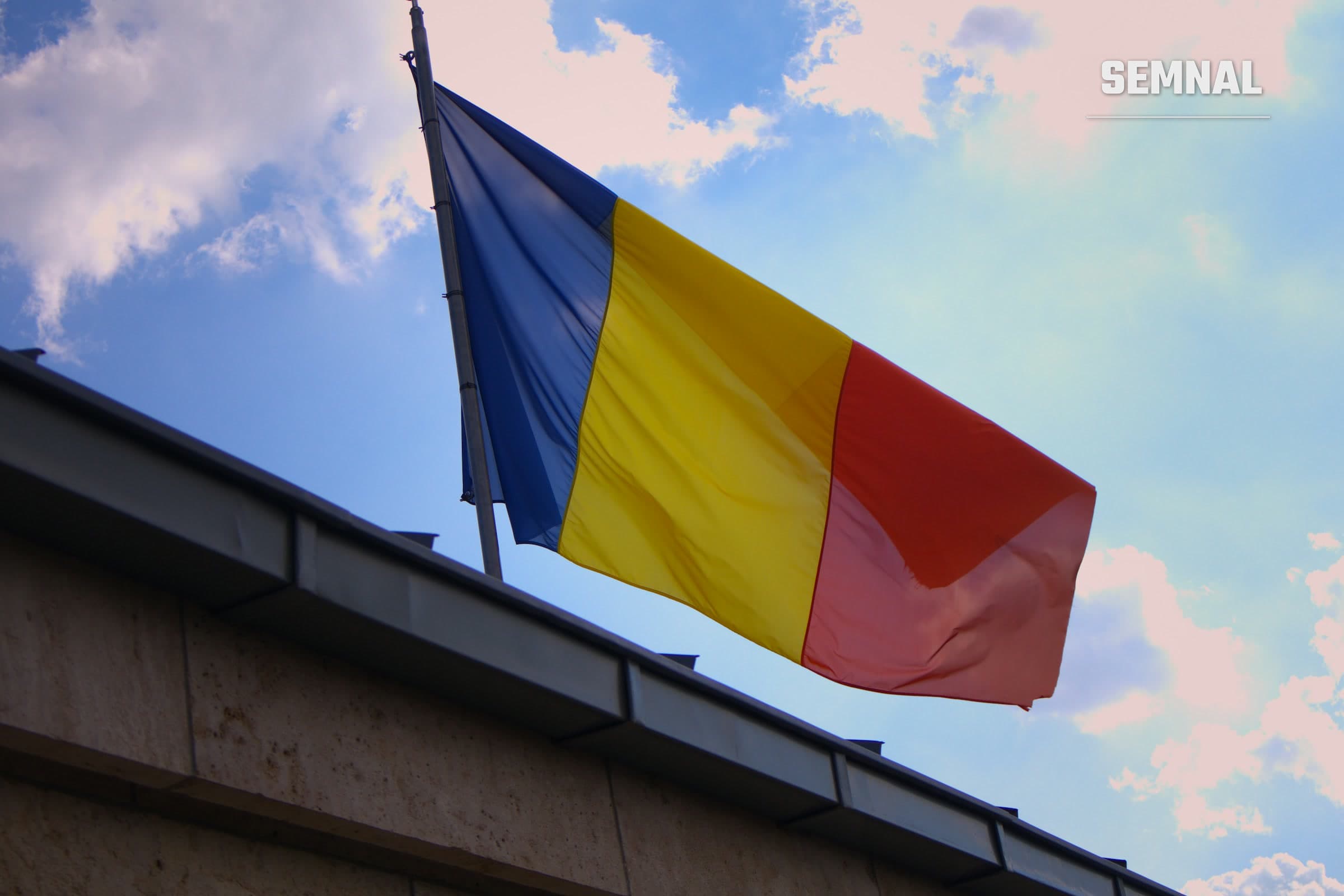 Drapelul României fluturând pe cer senin, deasupra unei clădiri