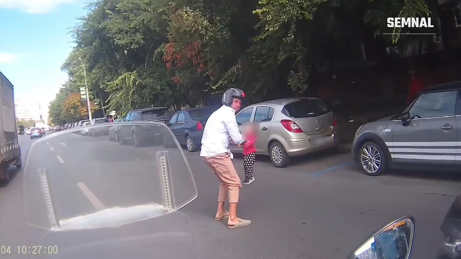 Un scuterist ține de mână o fetiță mică pe carosabil, pe Șoseaua Mihai Bravu din București