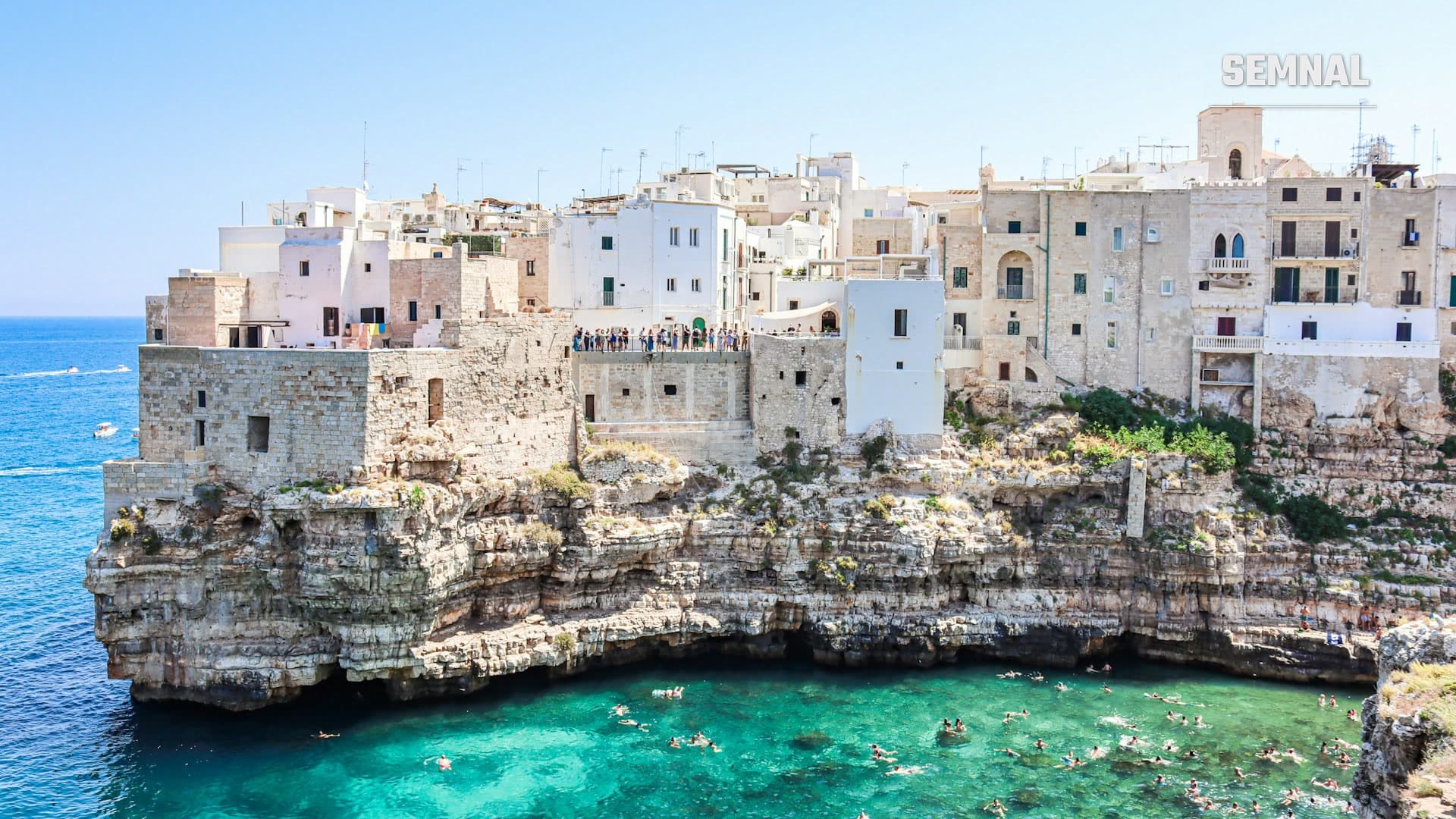 Case albe din calcar construite pe marginea falezei, deasupra mării turcoaz, în Polignano a Mare, Italia