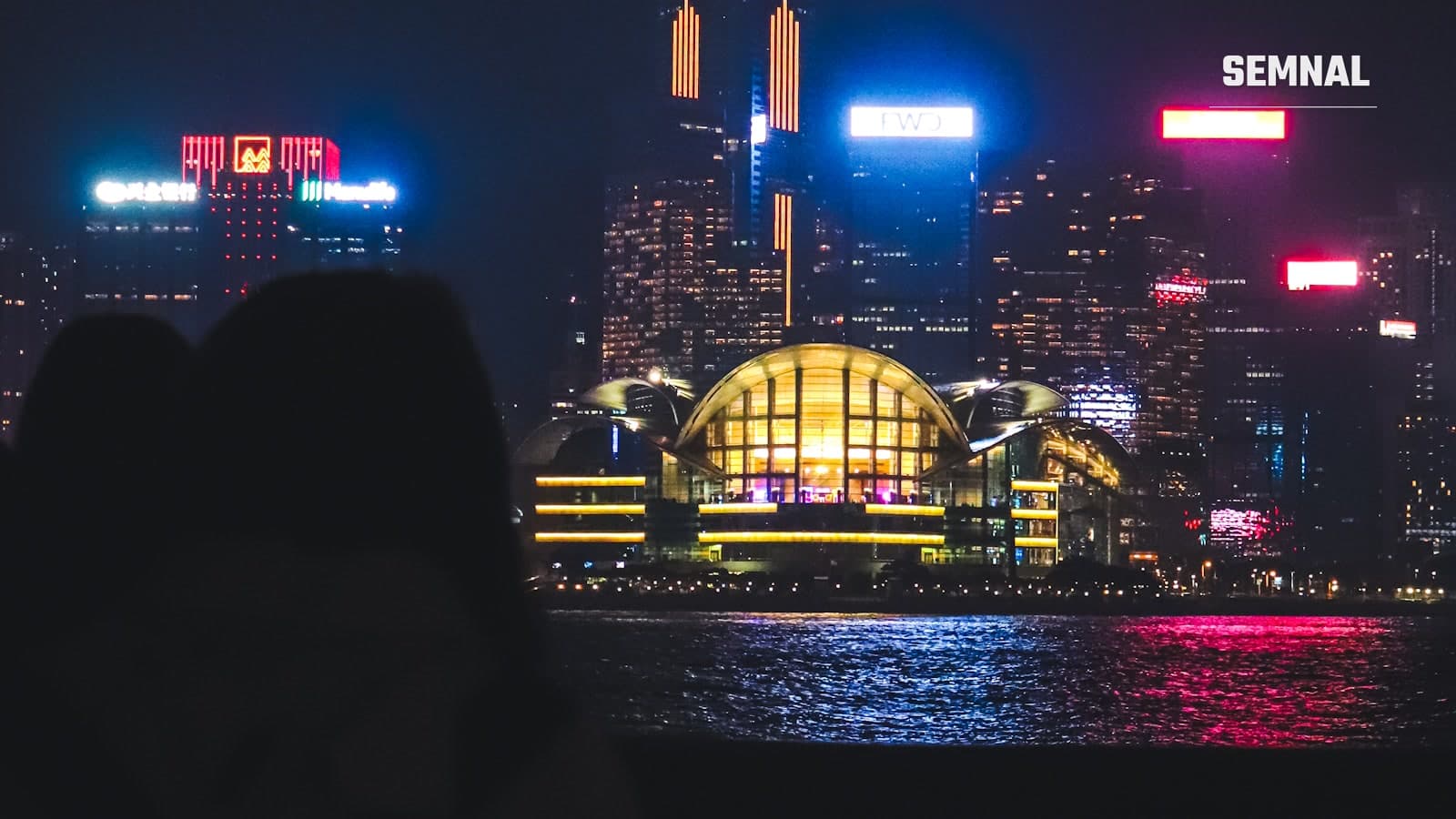 Priveliște nocturnă a golfului Victoria Harbour din Hong Kong, cu zgârie-norii cartierului financiar iluminați