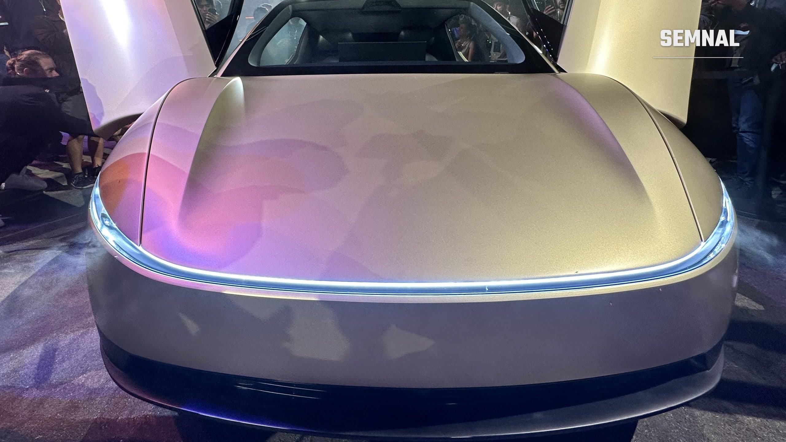 Fața unui Tesla Cybercab auriu, cu ambele uși tip fluture deschise, la o prezentare publică nocturnă, fără volan vizibil pe bord