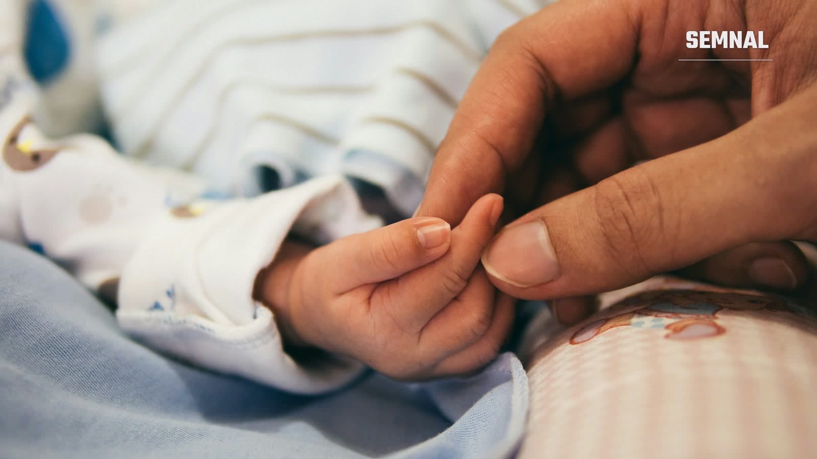 Mână de adult ținând cu blândețe degetul unui nou-născut, simbol al unei nașteri și al legăturii dintre părinte și copil