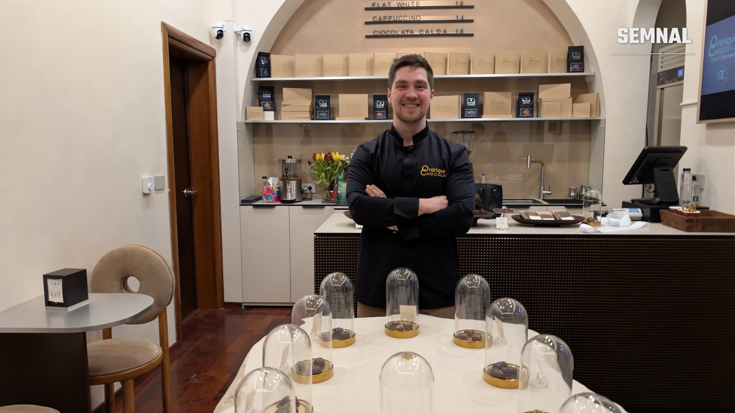 Dan Atudorai, cu mâinile încrucișate, în spatele tejghelei din ciocolateria Onirique din Iași, cu praline sub clopote de sticlă în prim-plan