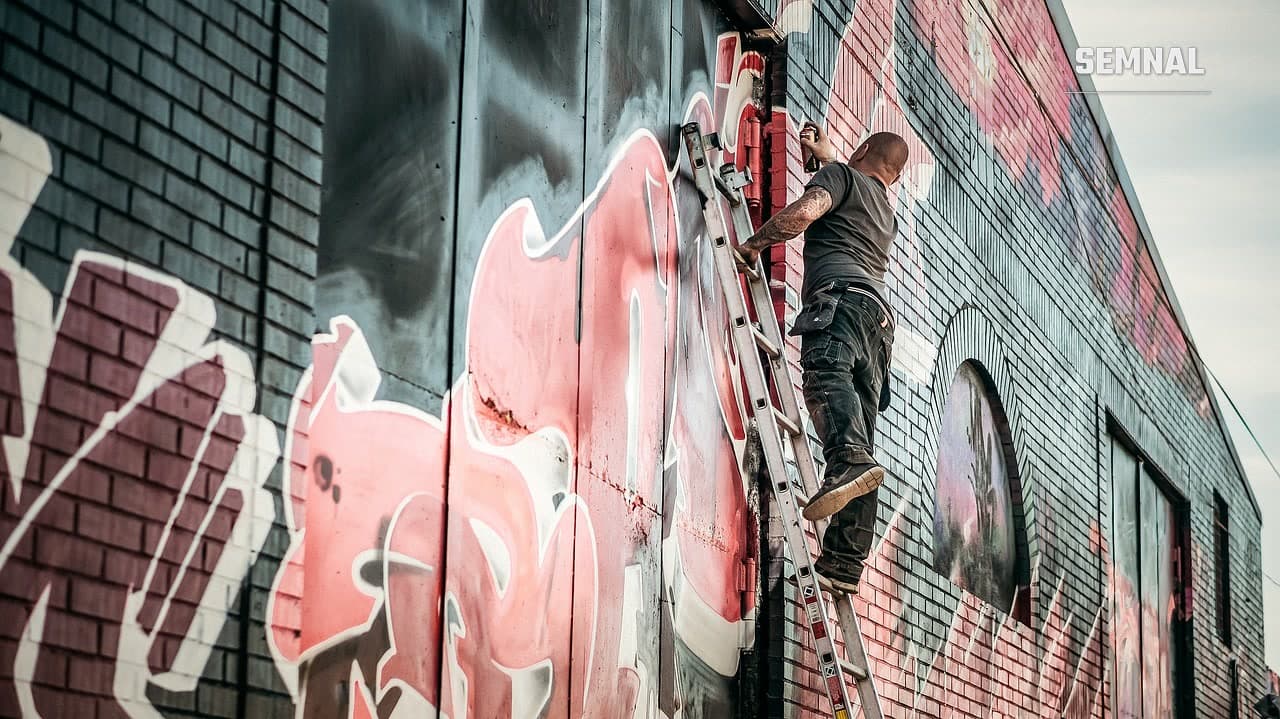 Artist pe o scară, pictând un mural mare pe zidul unei clădiri industriale, imagine ilustrativă ( foto Pixabay)