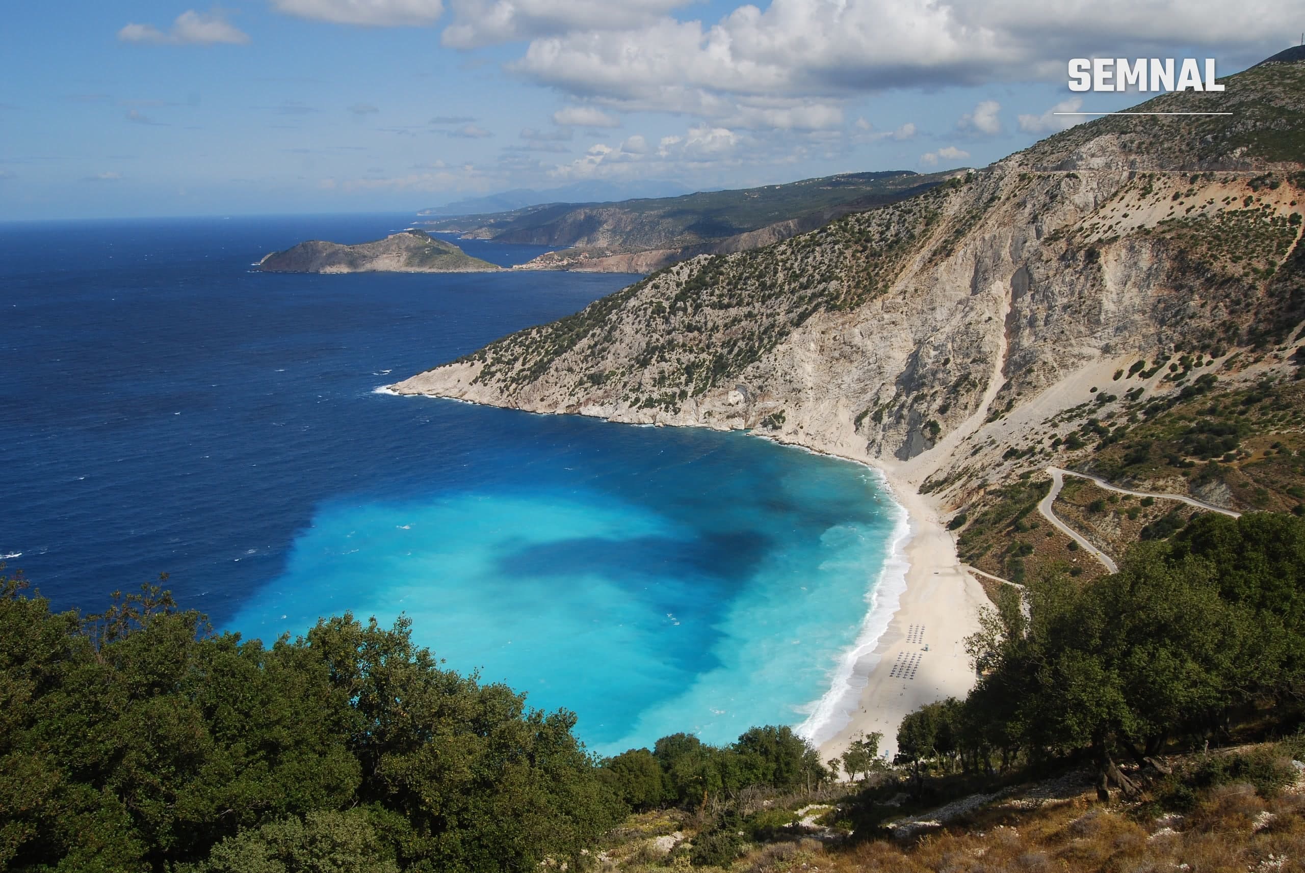 Vedere de sus a plajei Myrtos din Kefalonia, cu apă turcoaz și pietriș alb, mărginită de stânci calcaroase