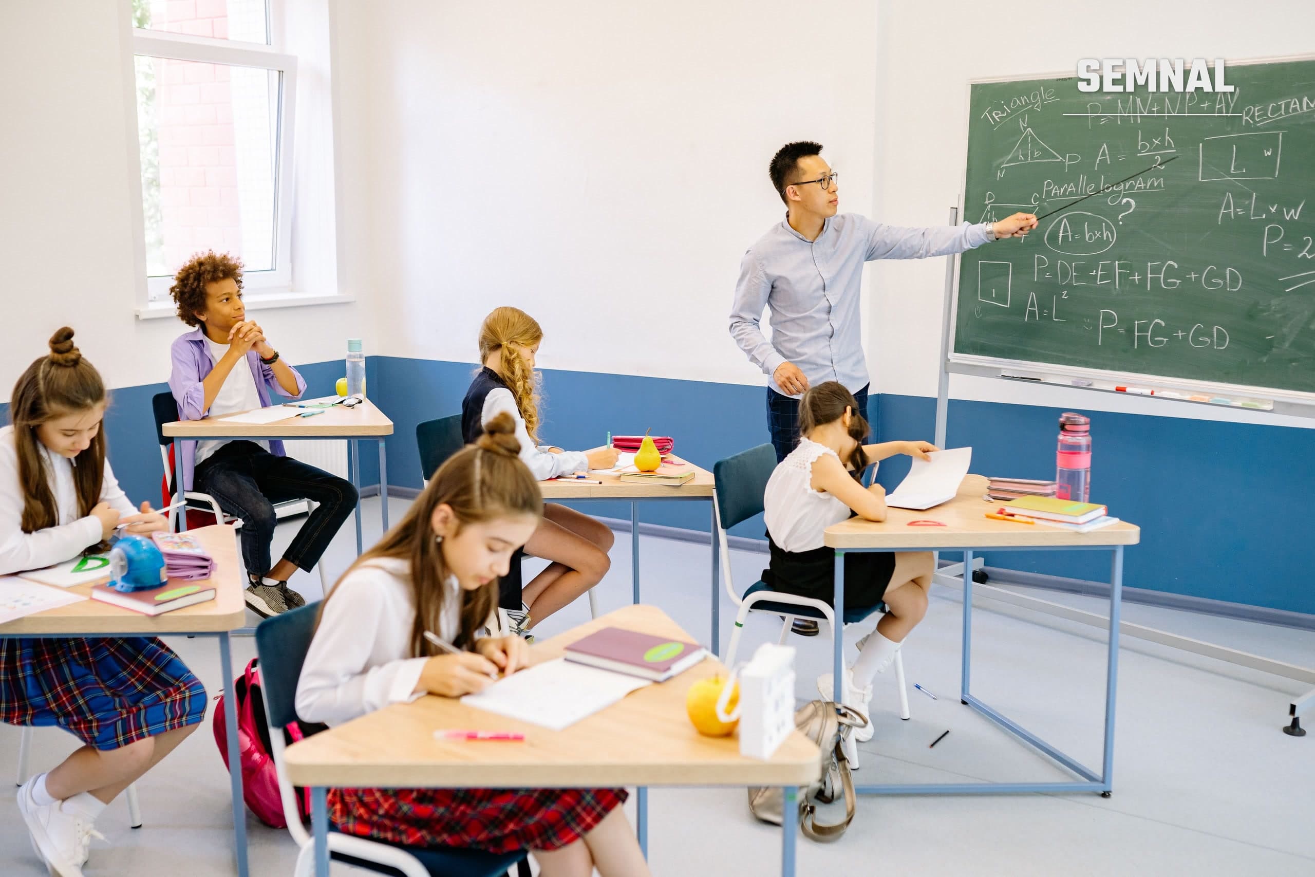 Profesor explică la tablă o problemă de matematică unor elevi așezați în bănci, într-o sală de clasă