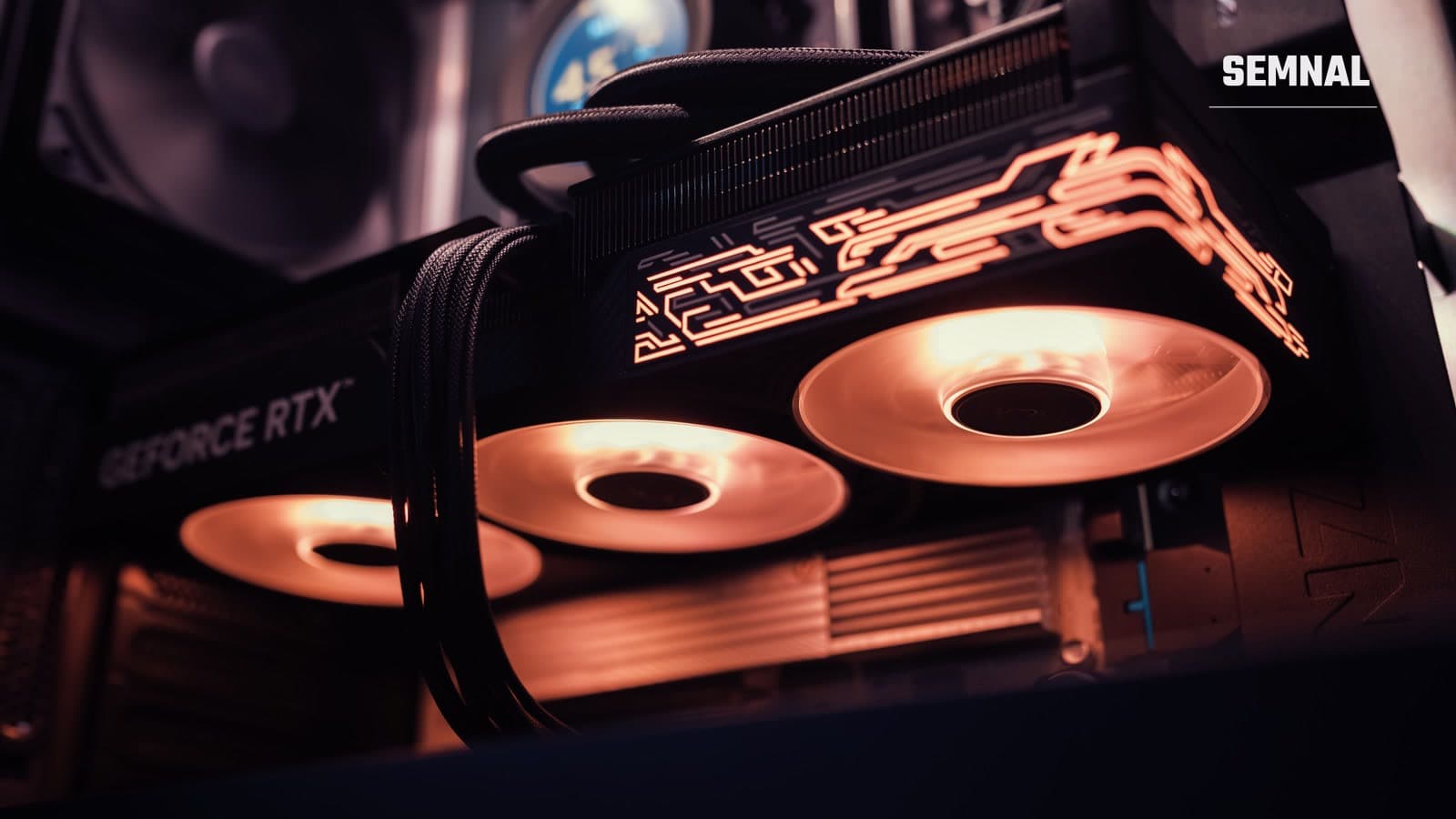 Placă video GeForce RTX cu iluminare RGB portocalie, montată într-o carcasă de calculator, cu trei ventilatoare vizibile