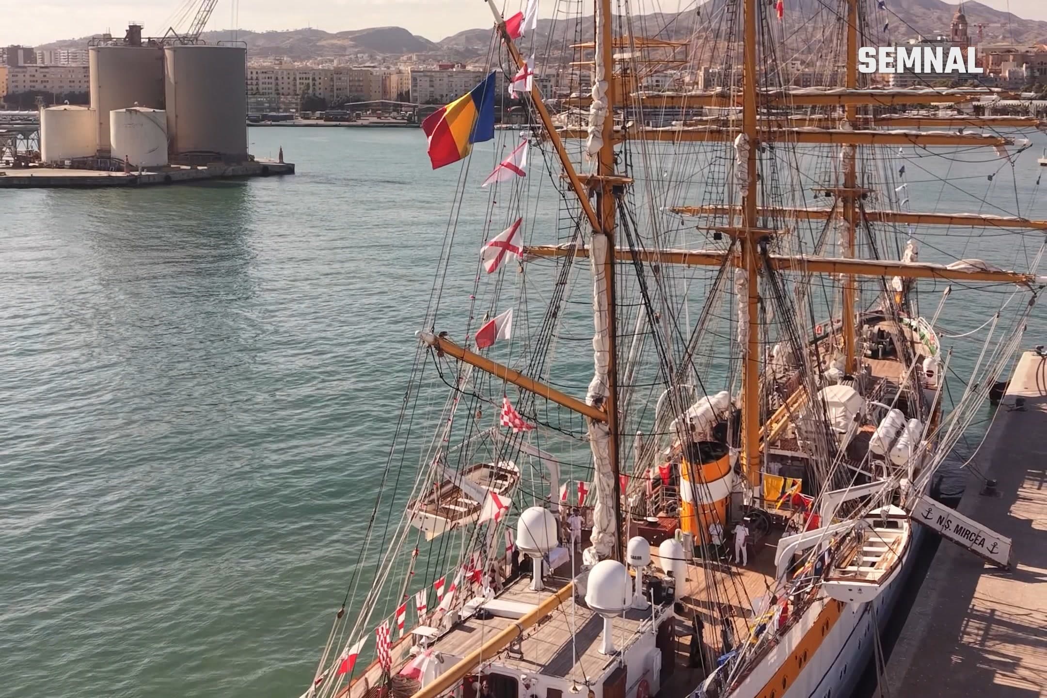 Nava-școală Mircea acostată în portul Málaga, cu marele pavoaz întins și tricolorul la arboret, pe fundalul orașului