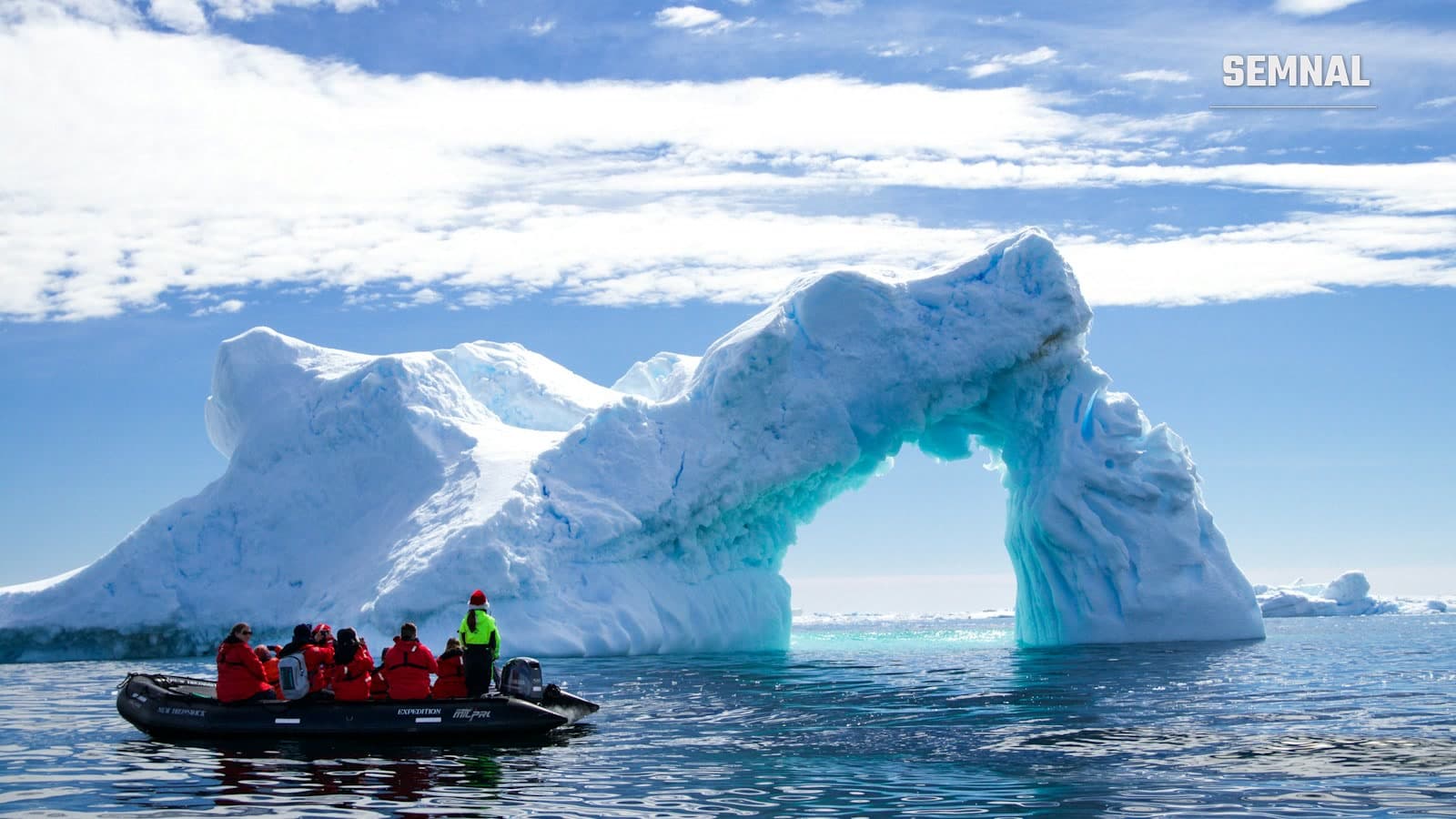 Turiști într-o barcă zodiac de expediție, în fața unui iceberg, în apele din Antarctica