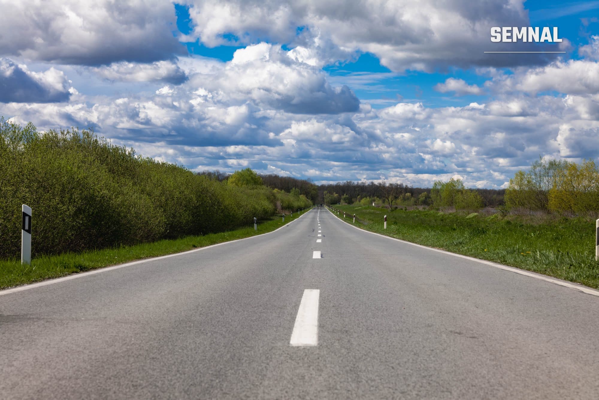 Autostradă asfaltată, dreaptă, flancată de câmpuri și pâlcuri de pădure, imagine ilustrativă