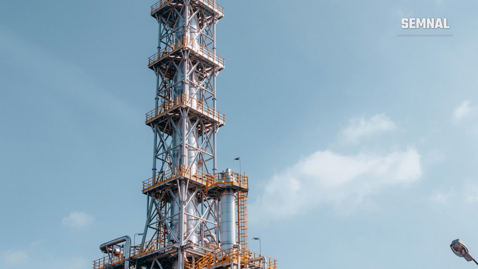 Turn de distilare la o rafinărie de petrol, cu conducte metalice și structuri industriale, sub cer înnorat