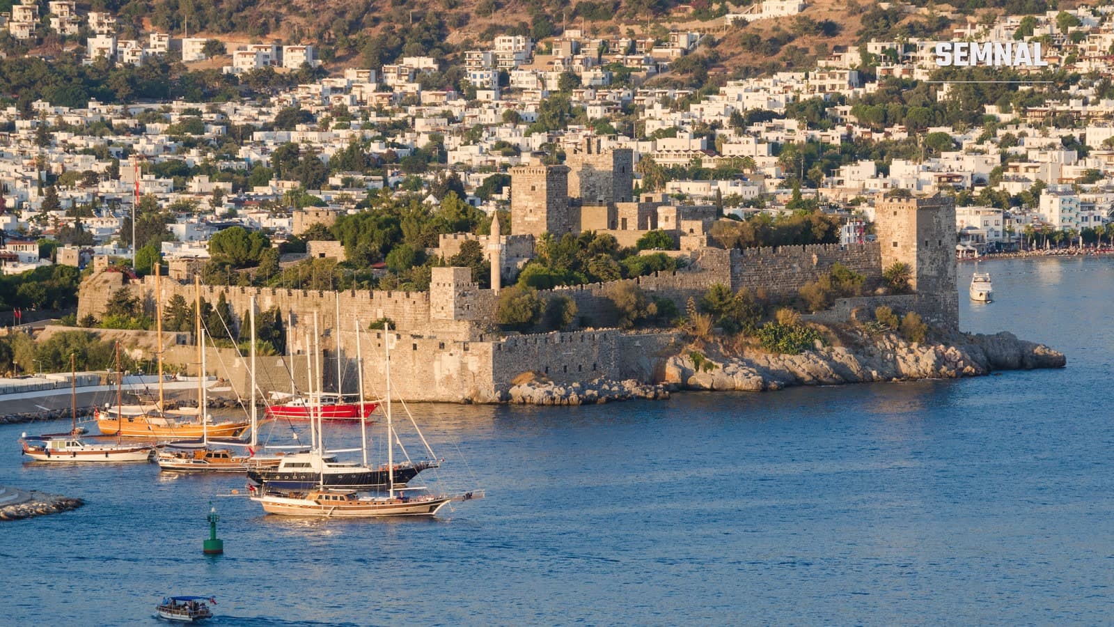 Castelul Bodrum, construit pe un promontoriu stâncos, cu gulete ancorate în port și orașul cu case albe pe deal, în lumina serii