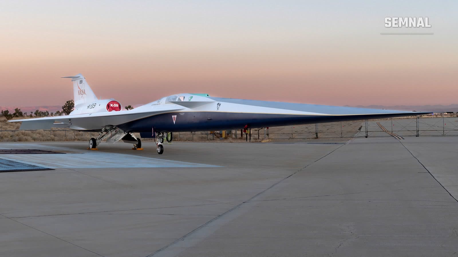 Avionul experimental supersonic X-59 al NASA, alb cu albastru, cu botul lung și ascuțit, staționat pe platformă la răsărit, cu cerul roz în fundal