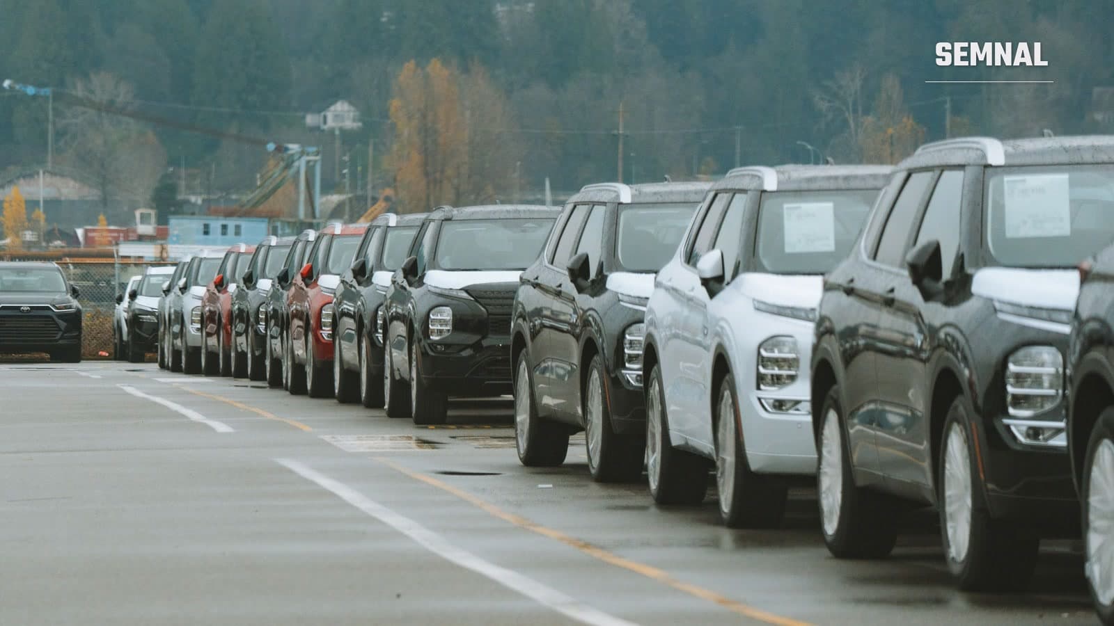 Rând de SUV-uri noi, negre, albe și roșii, parcate unul lângă altul pe un platou exterior, cu autocolante pe parbriz, într-o zi înnorată