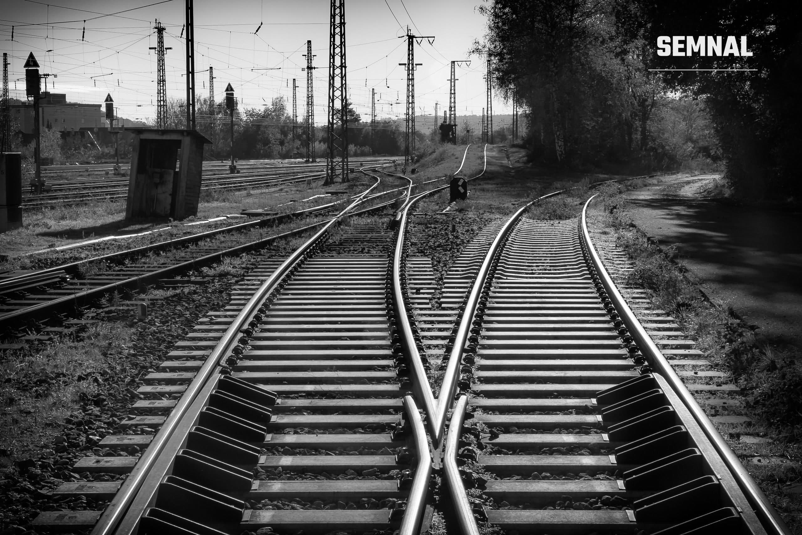 Șine de cale ferată la o intersecție, imagine alb-negru, ilustrativă