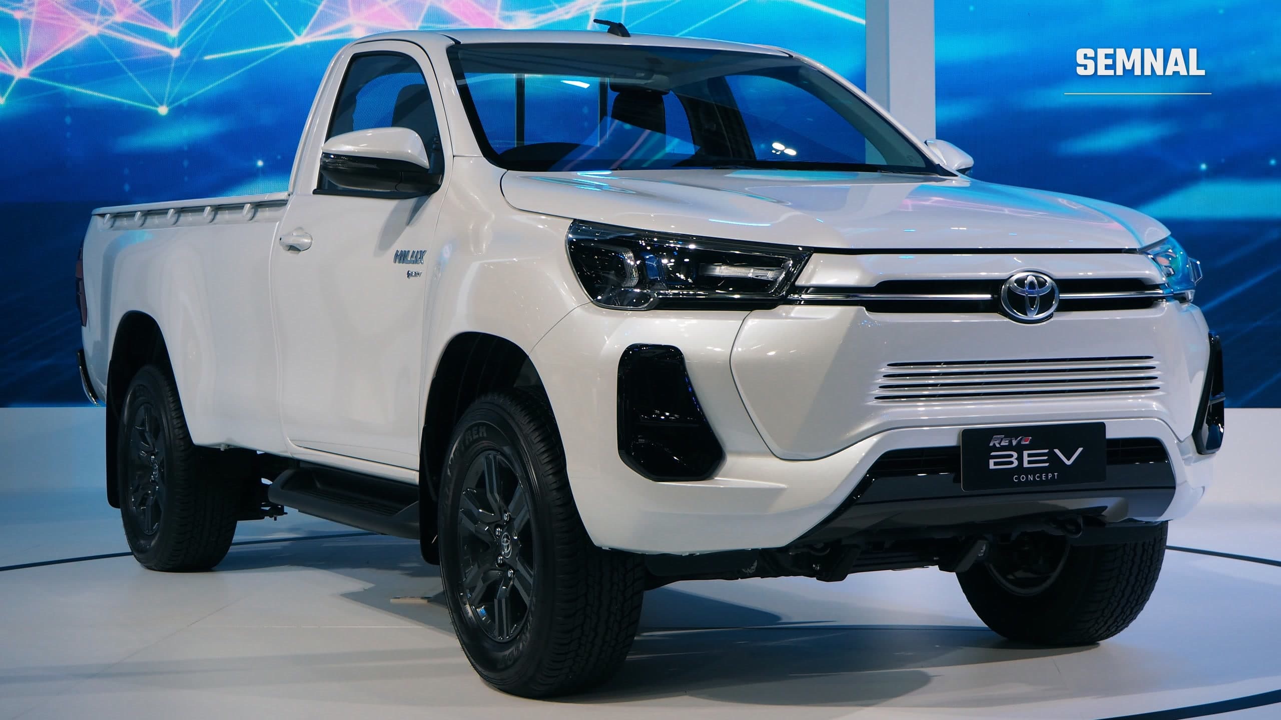 Prototipul electric Toyota Hilux Revo BEV Concept, un pick-up alb expus pe un podium la un salon auto din Thailanda