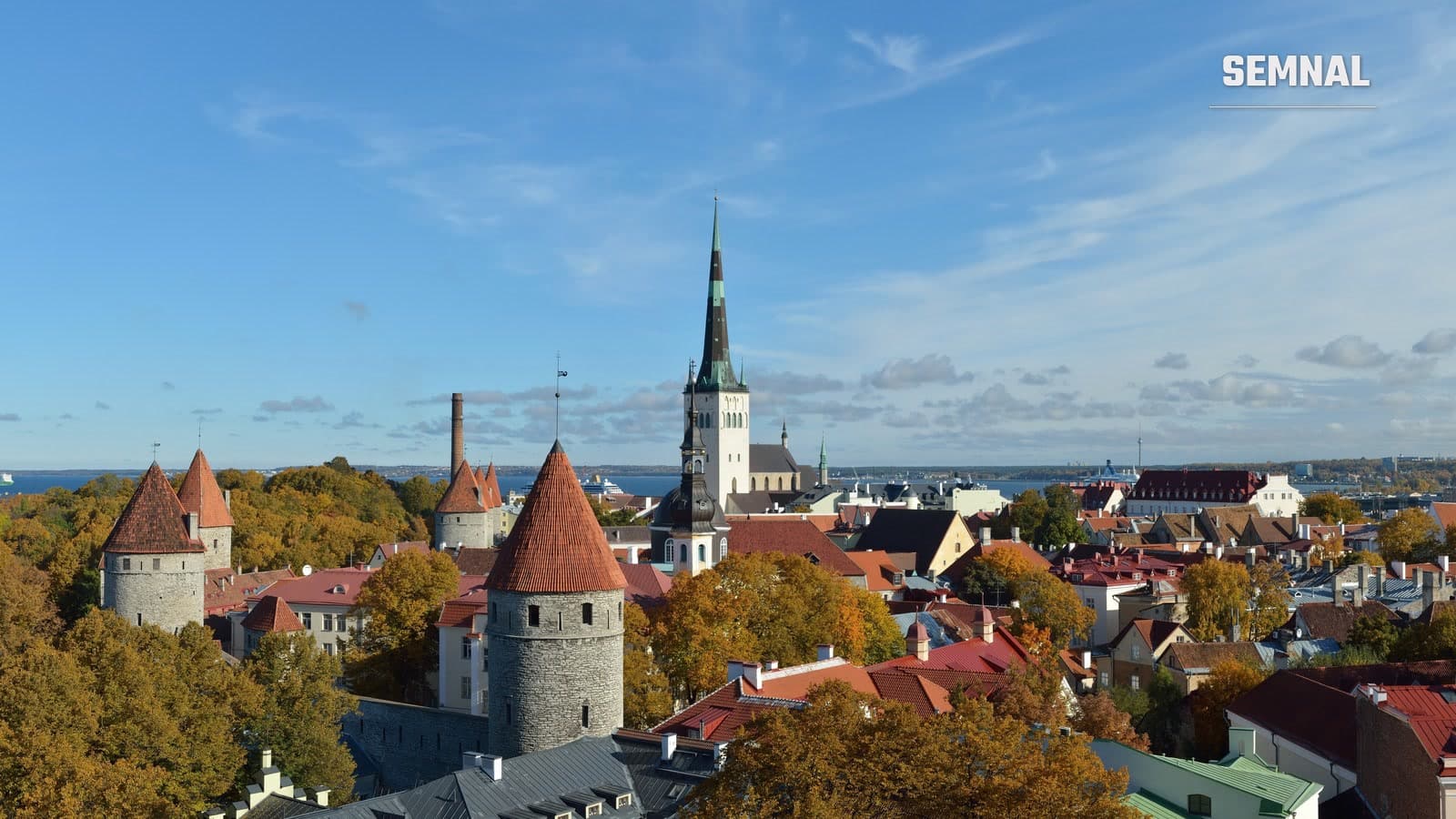 Panoramă a centrului vechi din Tallinn: turnuri medievale de piatră cu acoperișuri roșii, turnul bisericii Sf. Olaf și casele orașului sub un cer senin