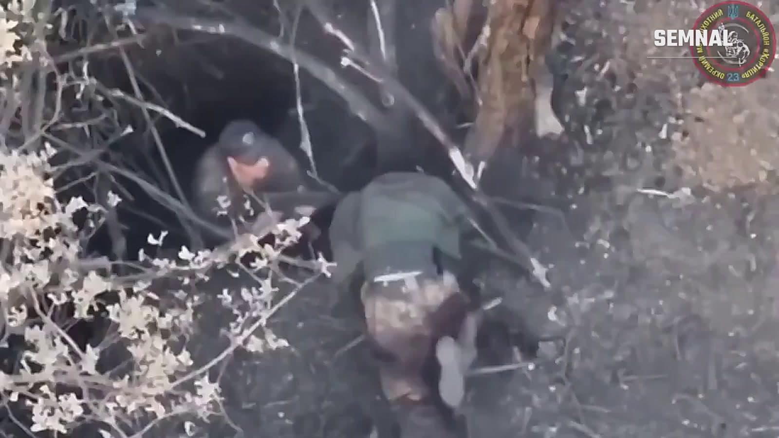 Imagine filmată de o dronă: un militar rus rănit, lângă intrarea unui adăpost săpat în pământ, ajutat de un alt militar