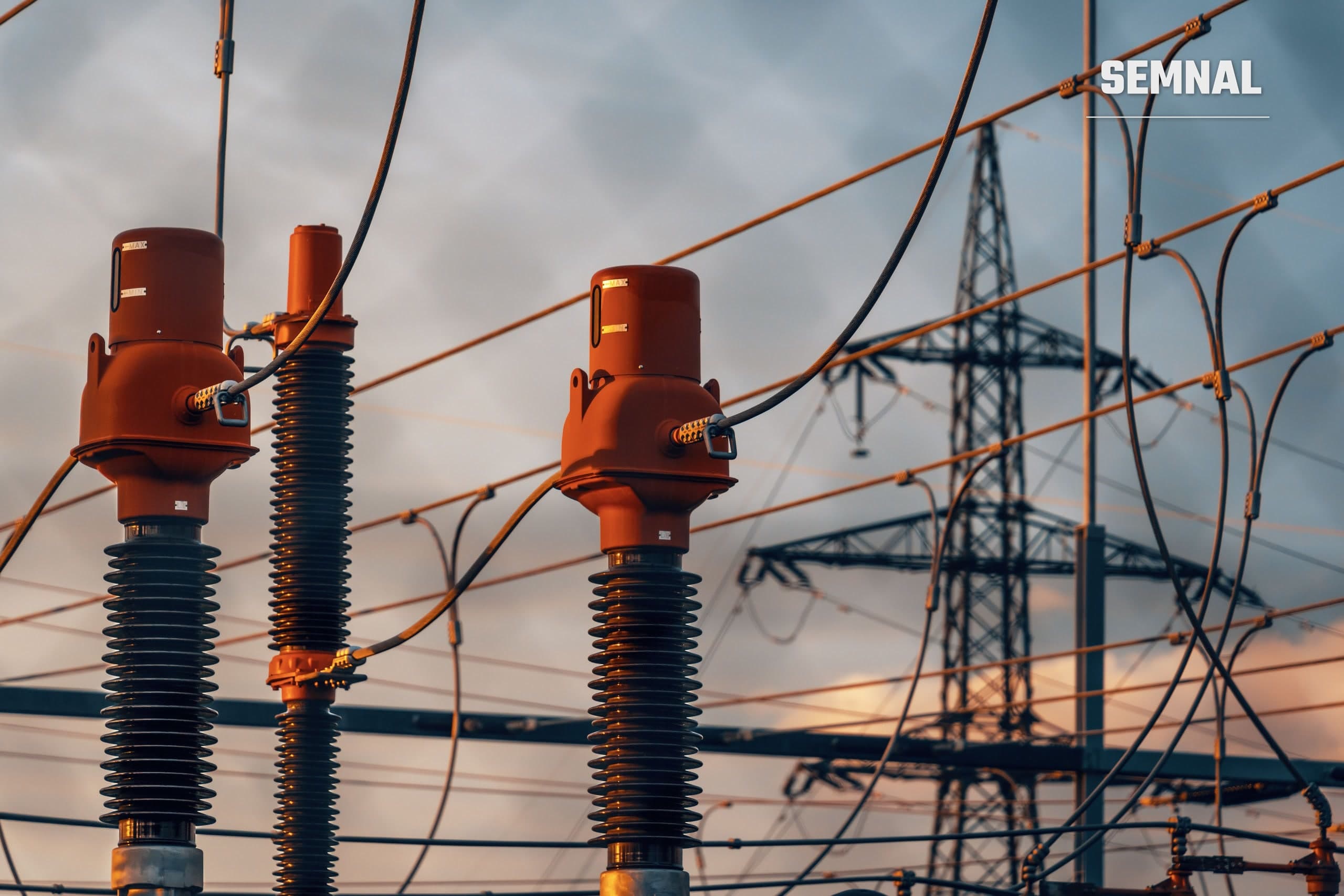 Echipamente dintr-o stație electrică de înaltă tensiune, cu un stâlp de transport al energiei în fundal, imagine ilustrativă