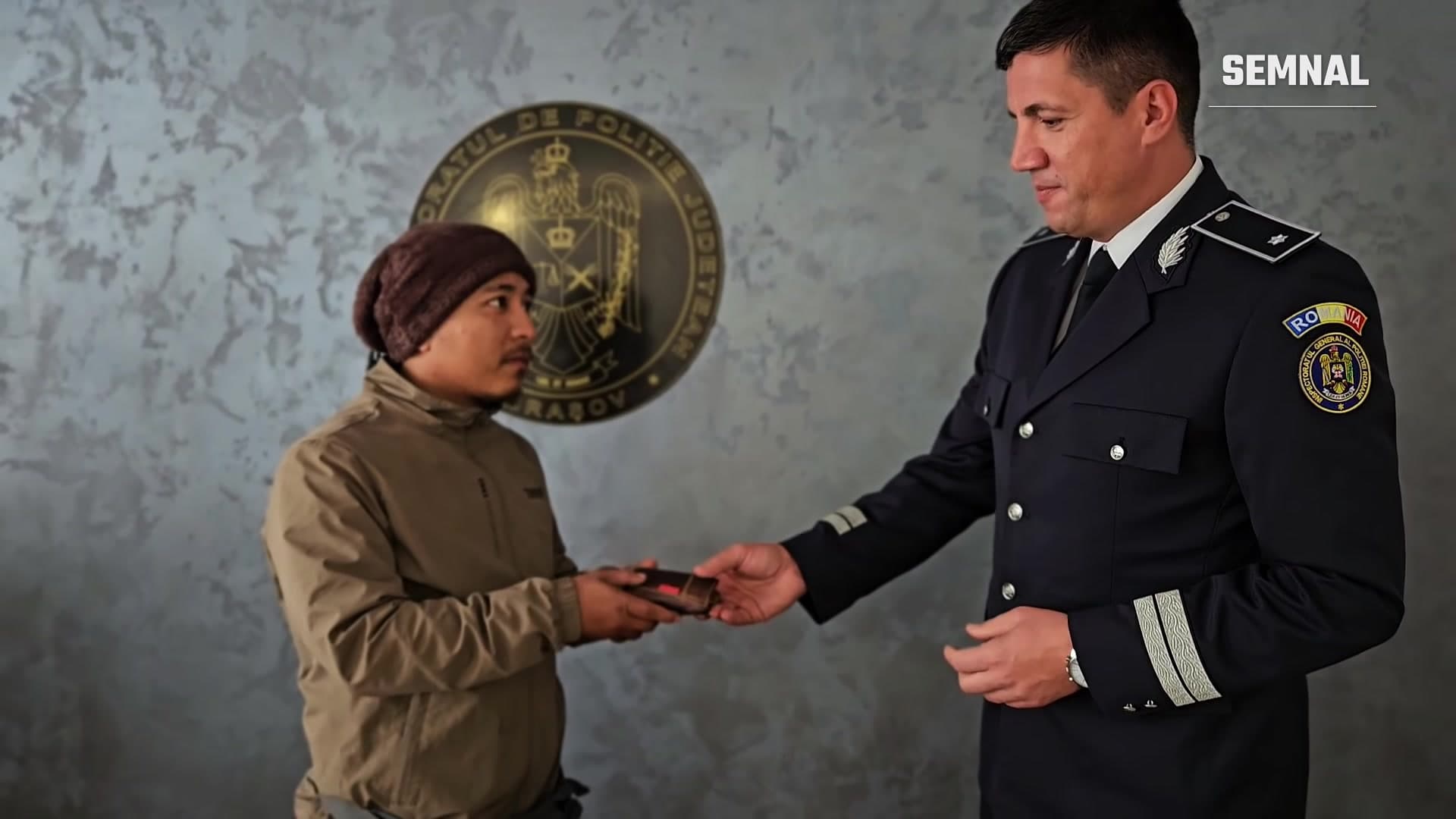 Polițist din Brașov înmânând portofelul unui bărbat din Nepal, în fața emblemei Inspectoratului de Poliție Județean Brașov