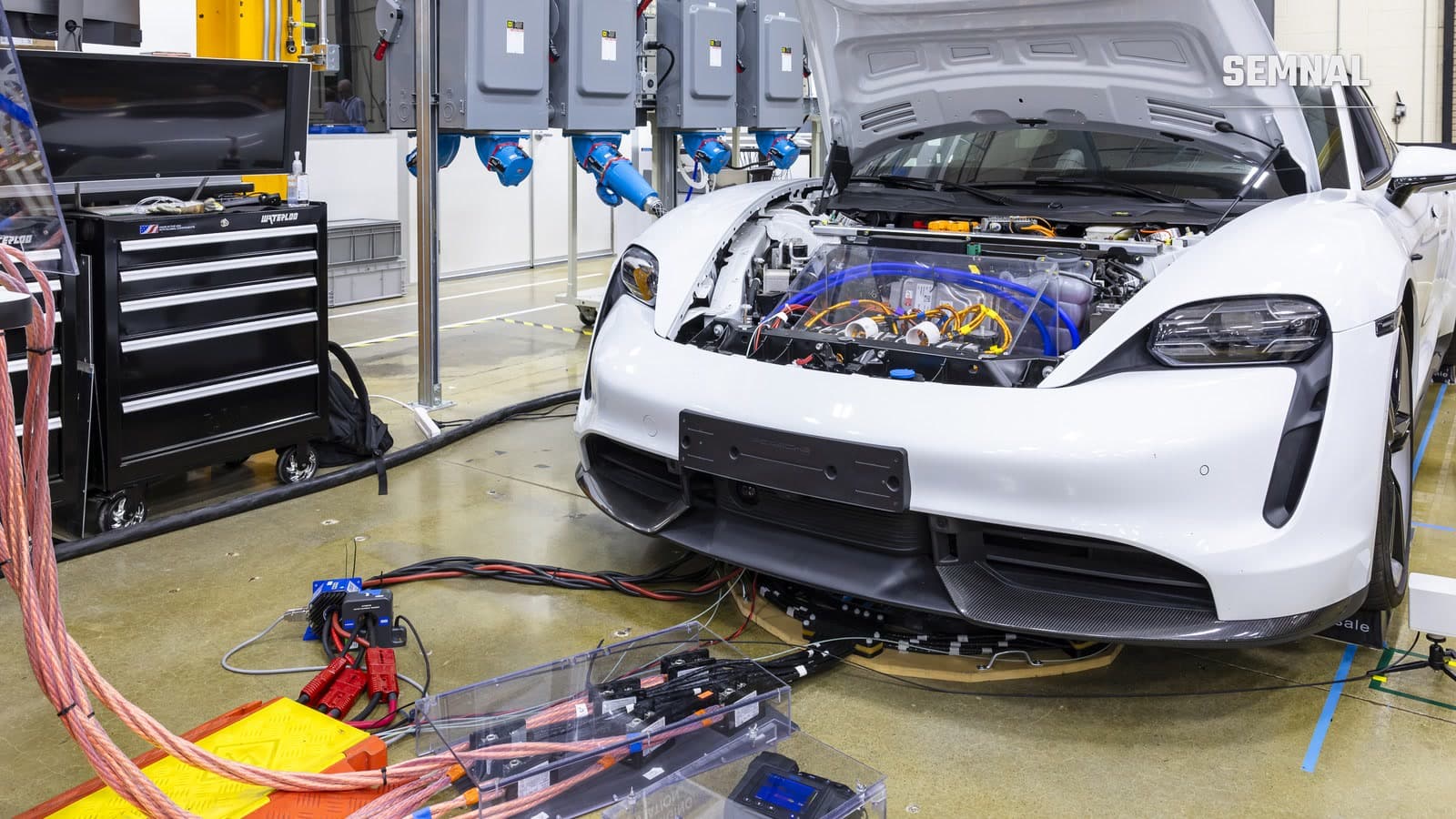 Porsche Taycan alb cu capota deschisă, conectat la cabluri și echipamente de măsurare într-un laborator, în timpul unui test de transfer wireless de 270 kW.
