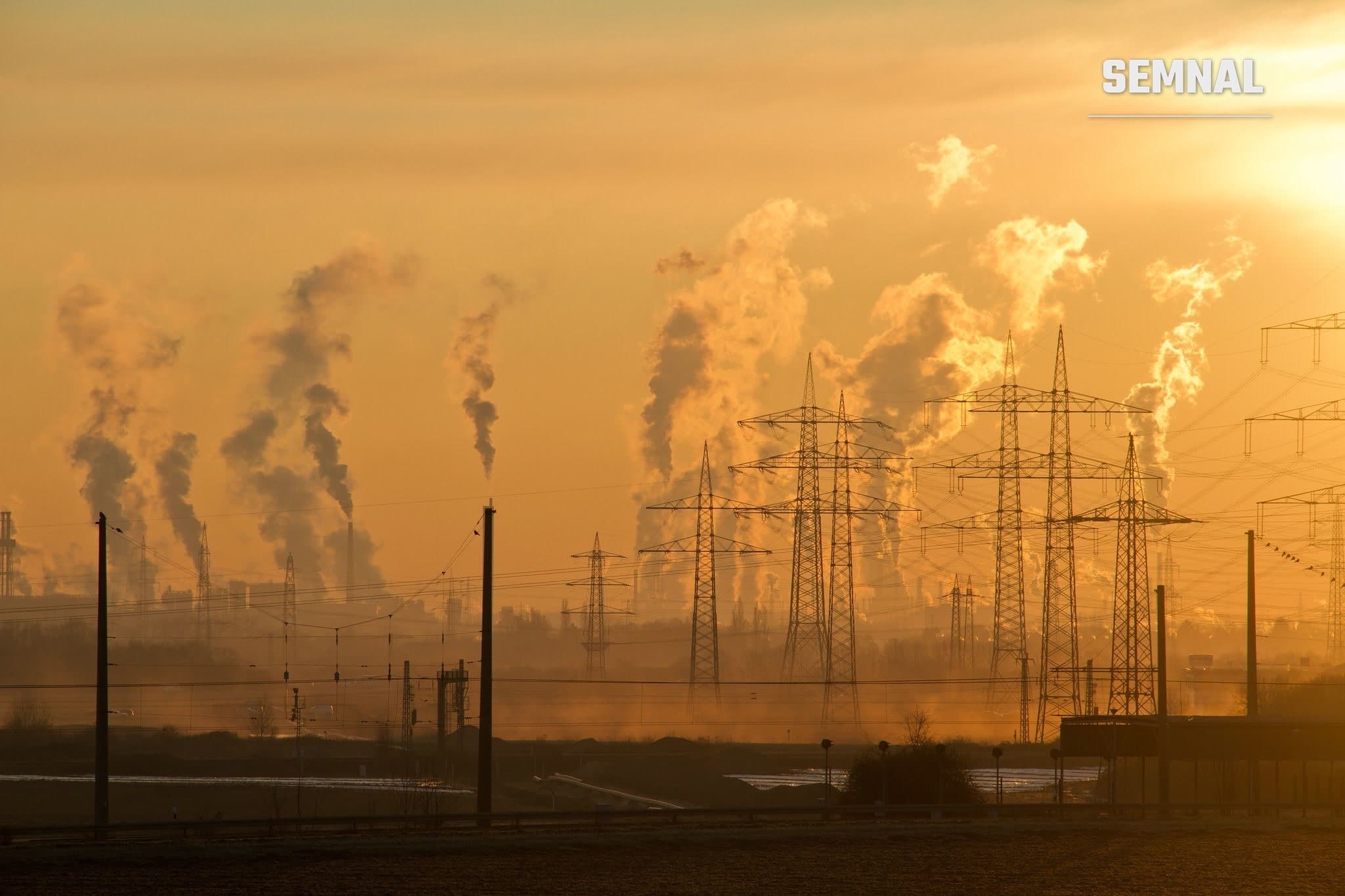 Siluetă de linii electrice și coșuri industriale care emit fum la apus, imagine ilustrativă pentru poluarea aerului