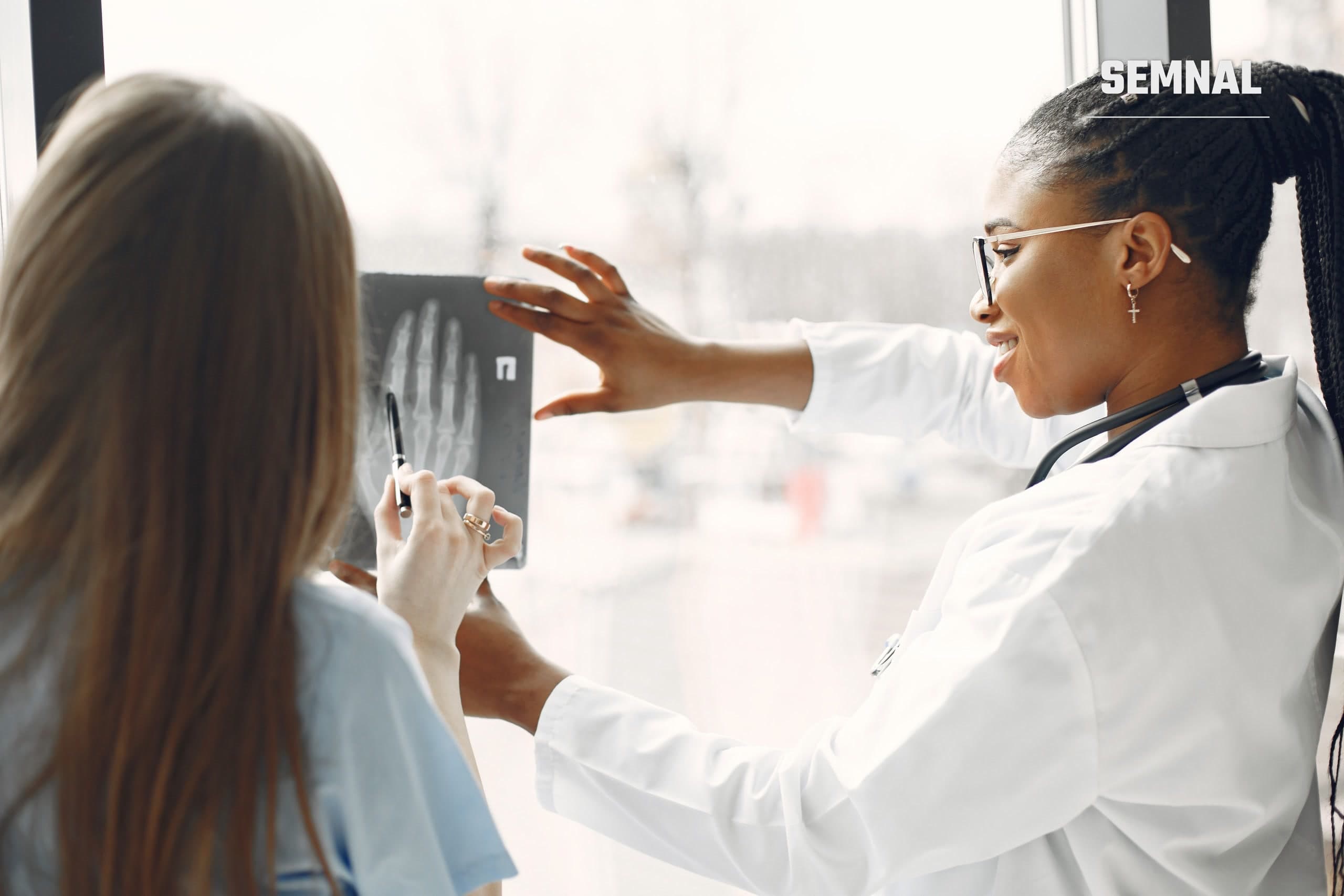 Doi medici analizează o radiografie lângă o fereastră, imagine ilustrativă pentru articolul despre osteoporoză și îmbătrânirea oaselor