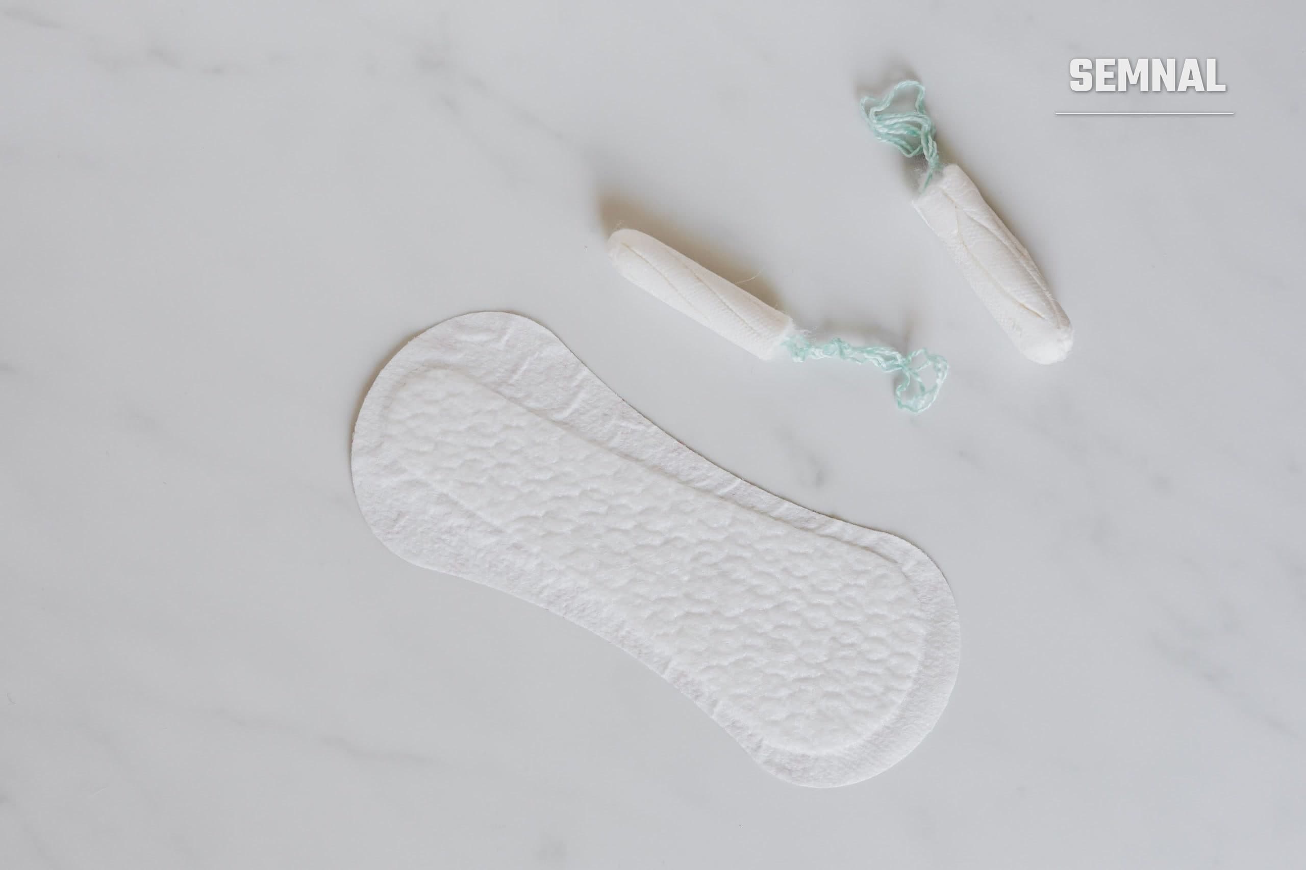 Absorbant igienic și două tampoane așezate pe o suprafață de marmură albă, văzute de sus (Foto: Karola G / Pexels)