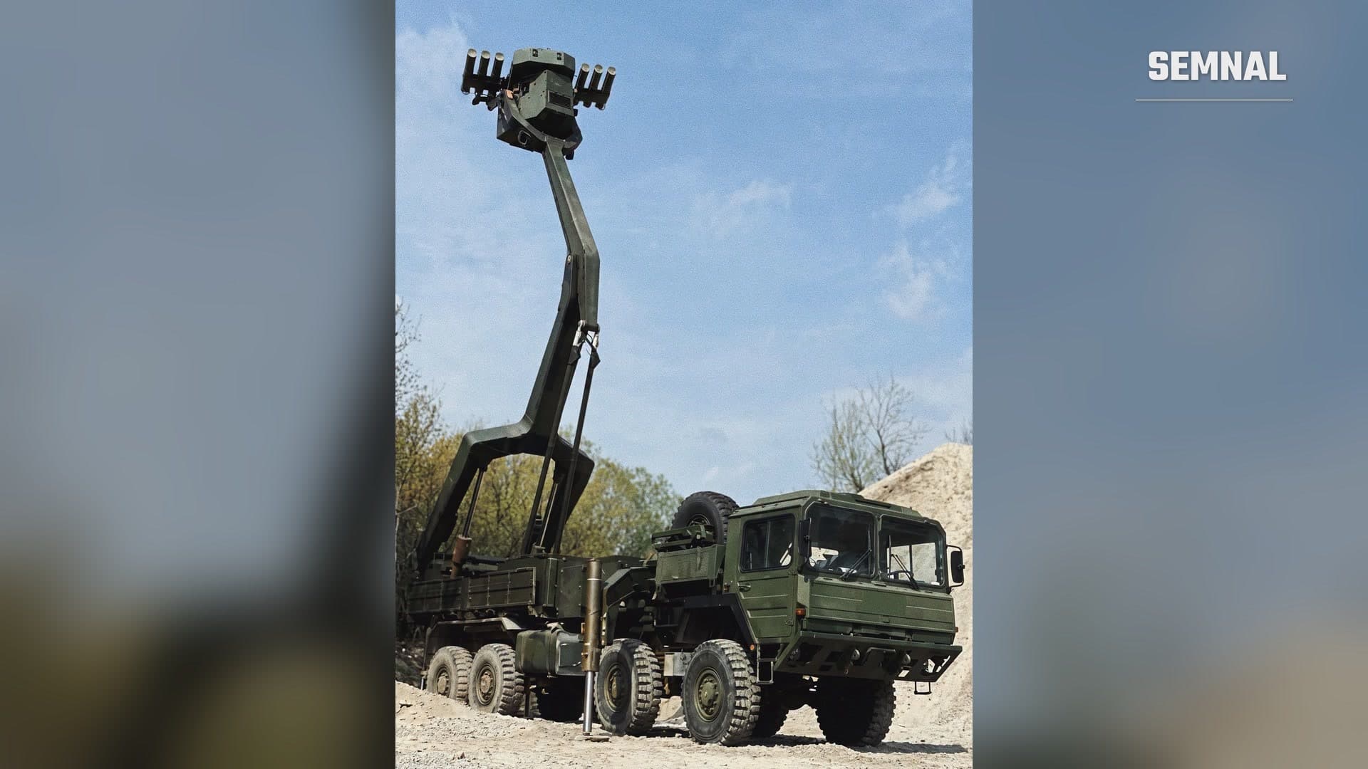 Camion militar MAN 8x8 cu braț articulat ridicat, purtând o cabină blindată cu tuburi de rachete antitanc HOT