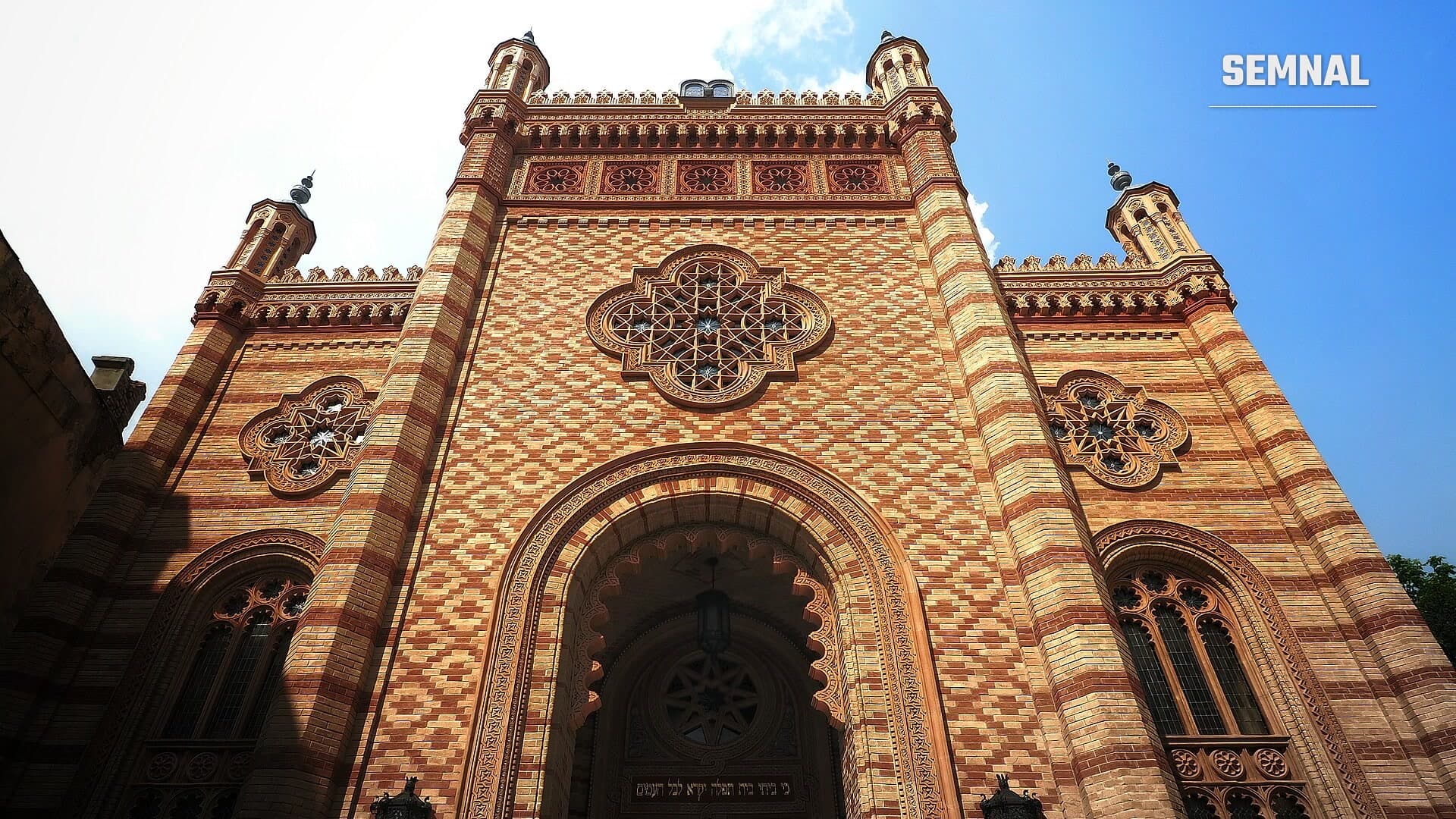 Fațada din cărămidă în două culori a Templului Coral din București, cu portal maur, rozete decorative și turnulețe de colț, văzută de jos