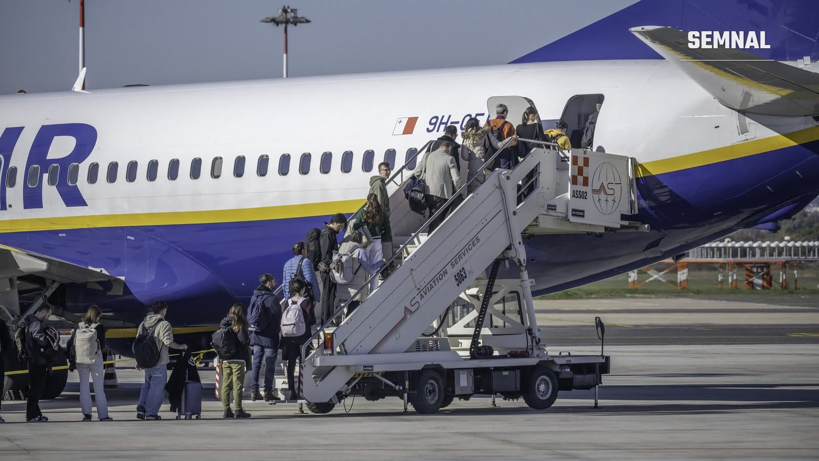 Pasageri cu rucsacuri și un troller urcă scara de îmbarcare a unui avion Boeing 737 pe platforma unui aeroport