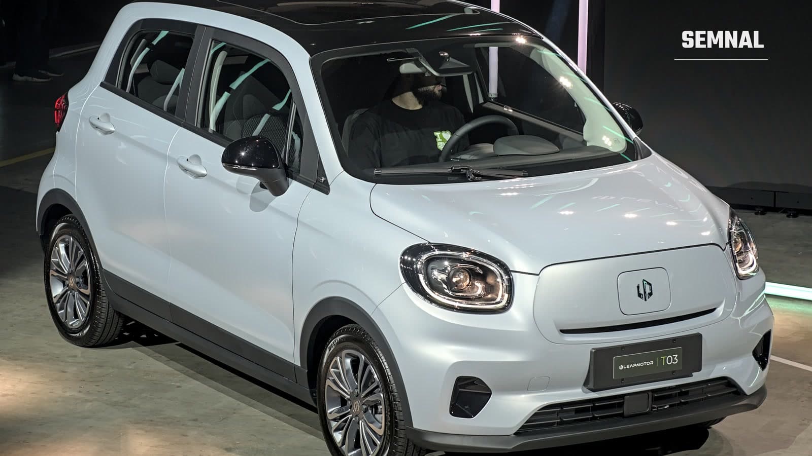 Leapmotor T03, mașină electrică de oraș alb-argintie, cu plafon negru, expusă la un salon auto, văzută din față și din lateral
