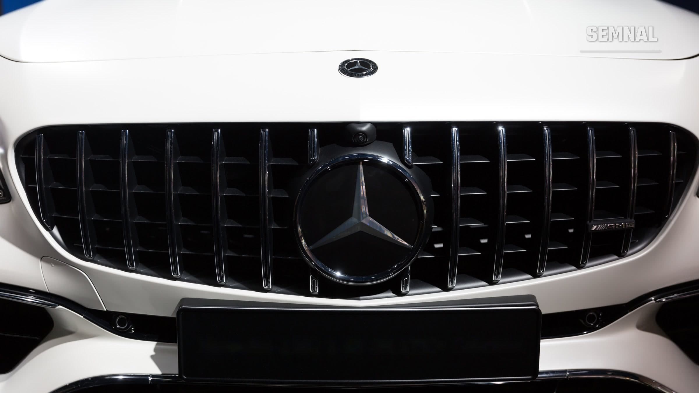 Steaua Mercedes-Benz pe grila neagră cu lamele verticale a unui Mercedes-AMG alb, văzută din față, cu o placă neagră goală dedesubt