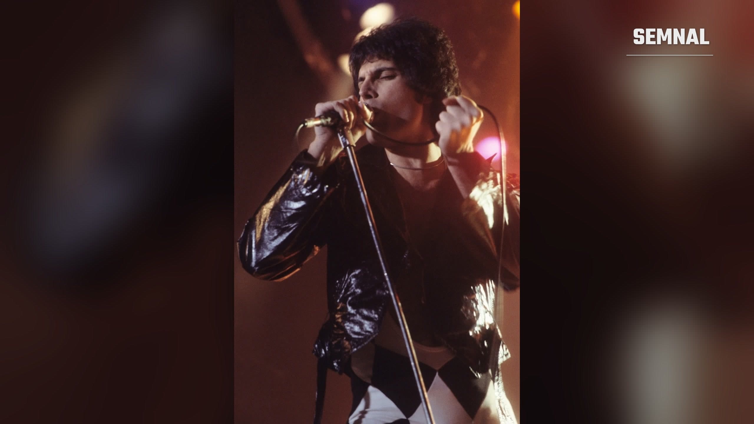 Freddie Mercury cântând la microfon, pe scenă, la un concert Queen, în New Haven, Connecticut, în noiembrie 1977