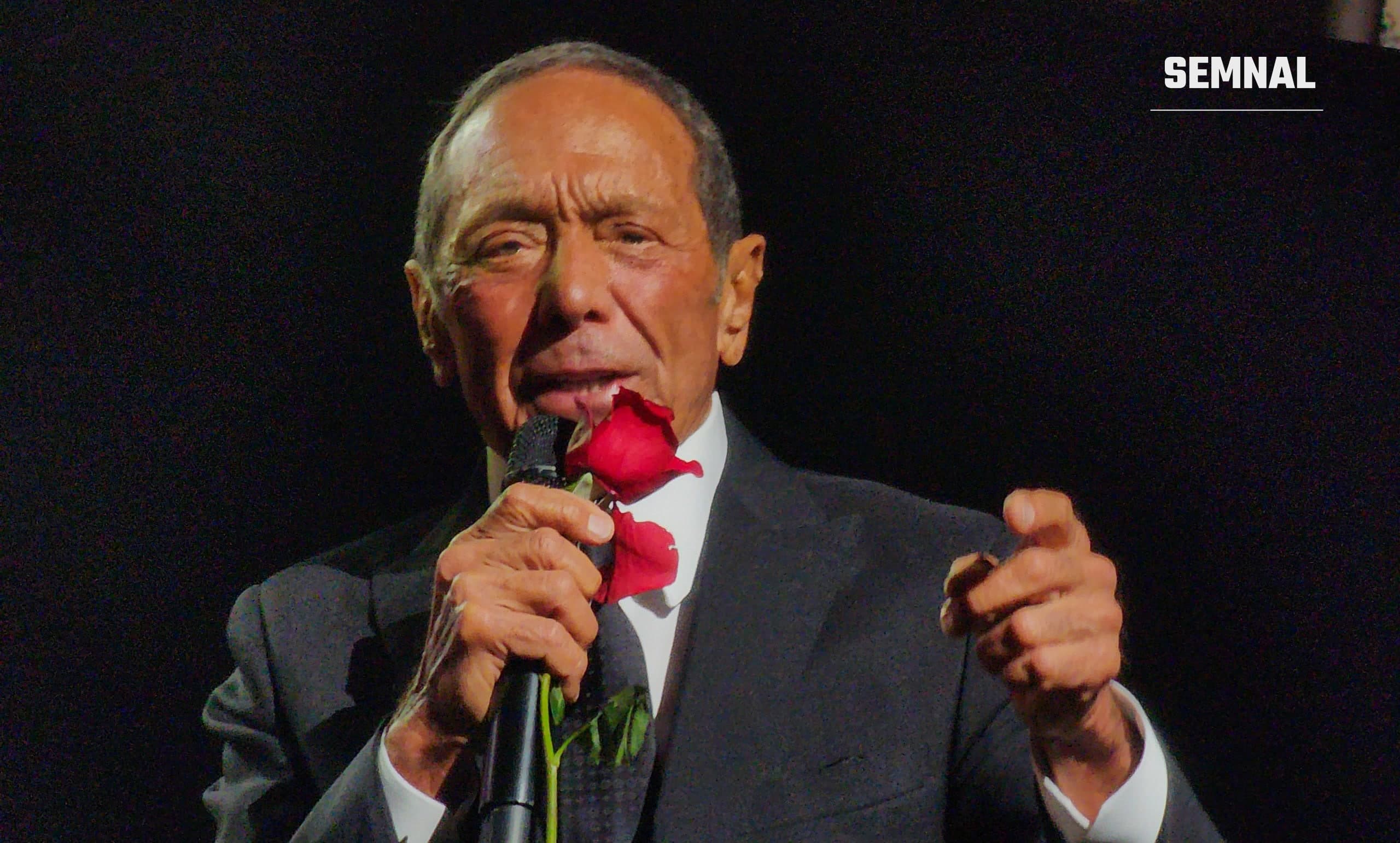 Paul Anka cântă pe scenă, cu un trandafir roșu și un microfon în mână, într-un concert din mai 2024 la Windsor, Ontario