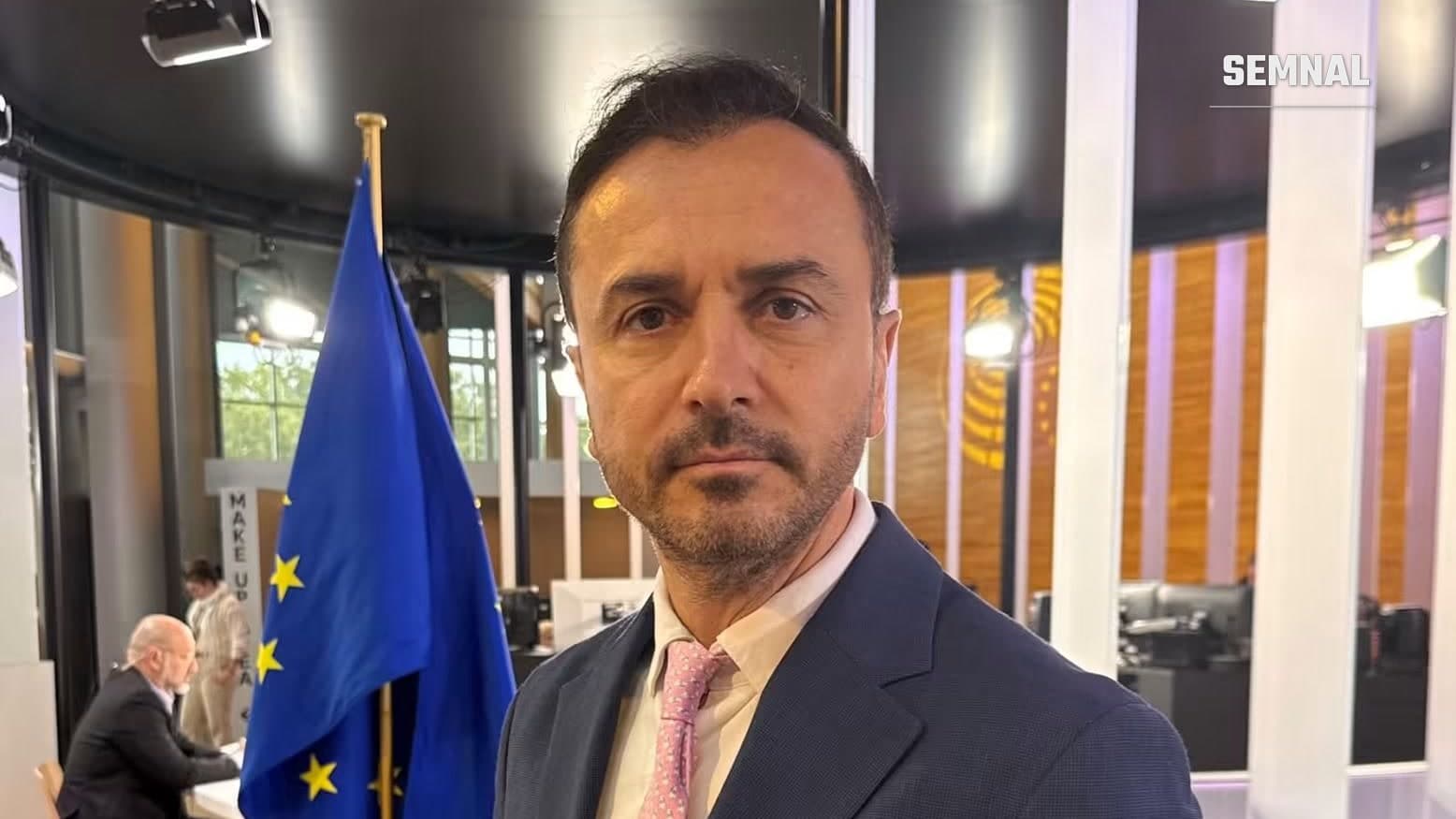 Eurodeputatul Ștefan Mușoiu în studioul Parlamentului European, lângă drapelul Uniunii Europene