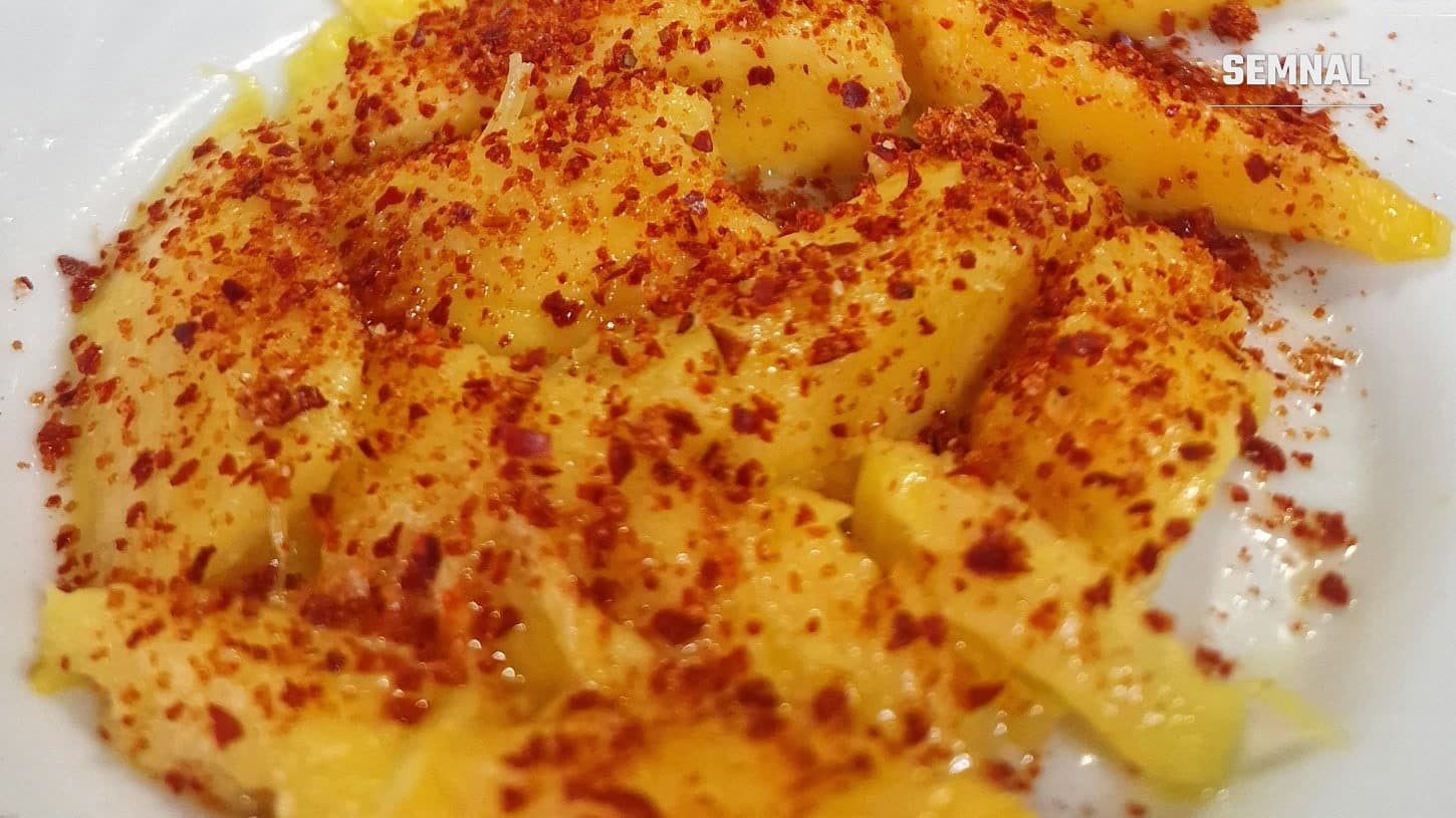 Felii de mango presărate cu condiment de chili, sare și lime, pe o farfurie albă
