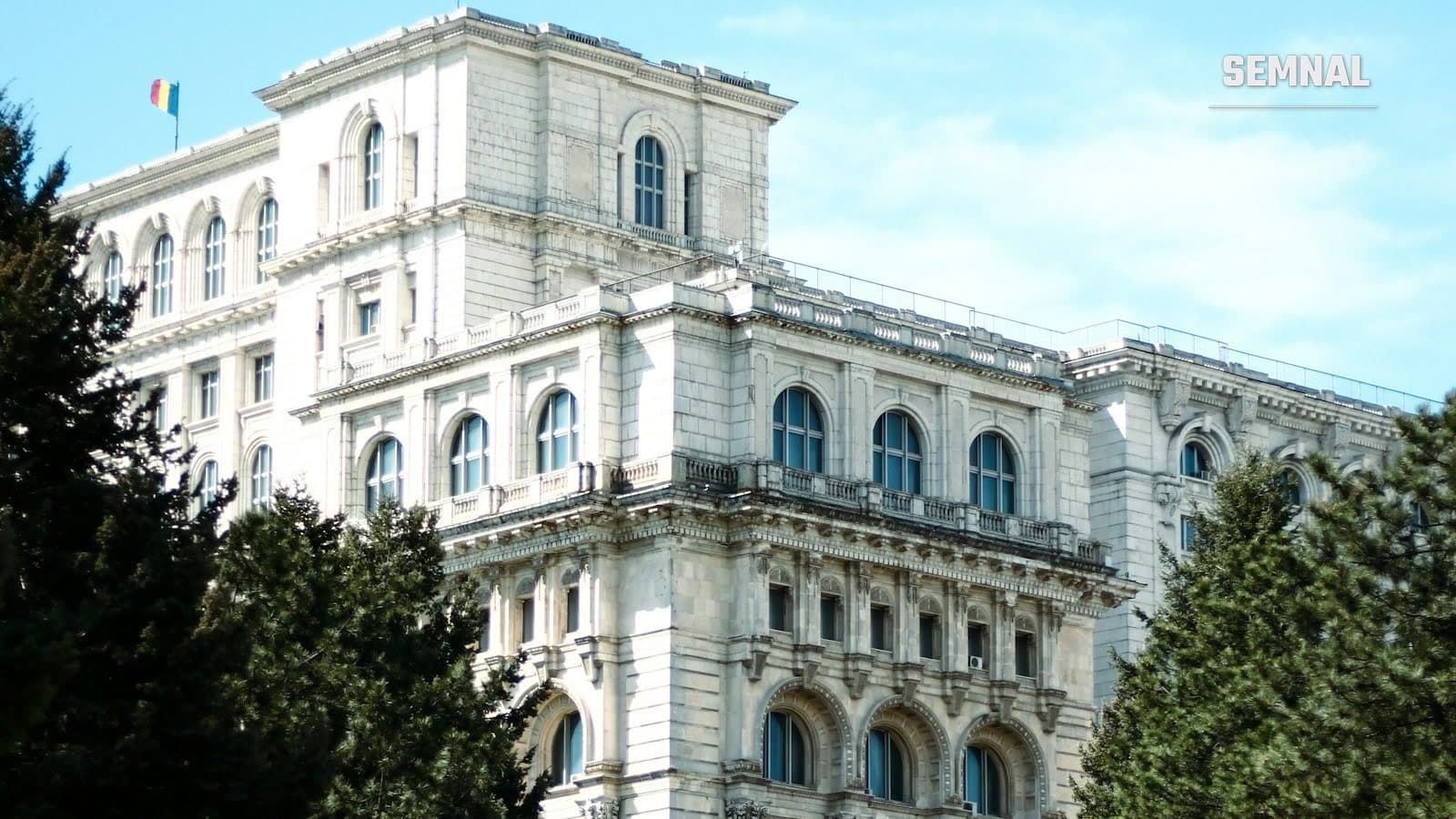 Palatul Parlamentului din București, văzut de pe o alee cu copaci, sub un cer senin