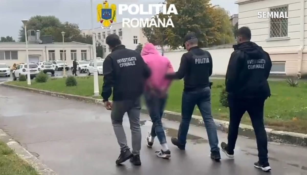 Polițiști din Constanța însoțesc un bărbat reținut, cu fața neclară, pe aleea din fața unei clădiri a poliției