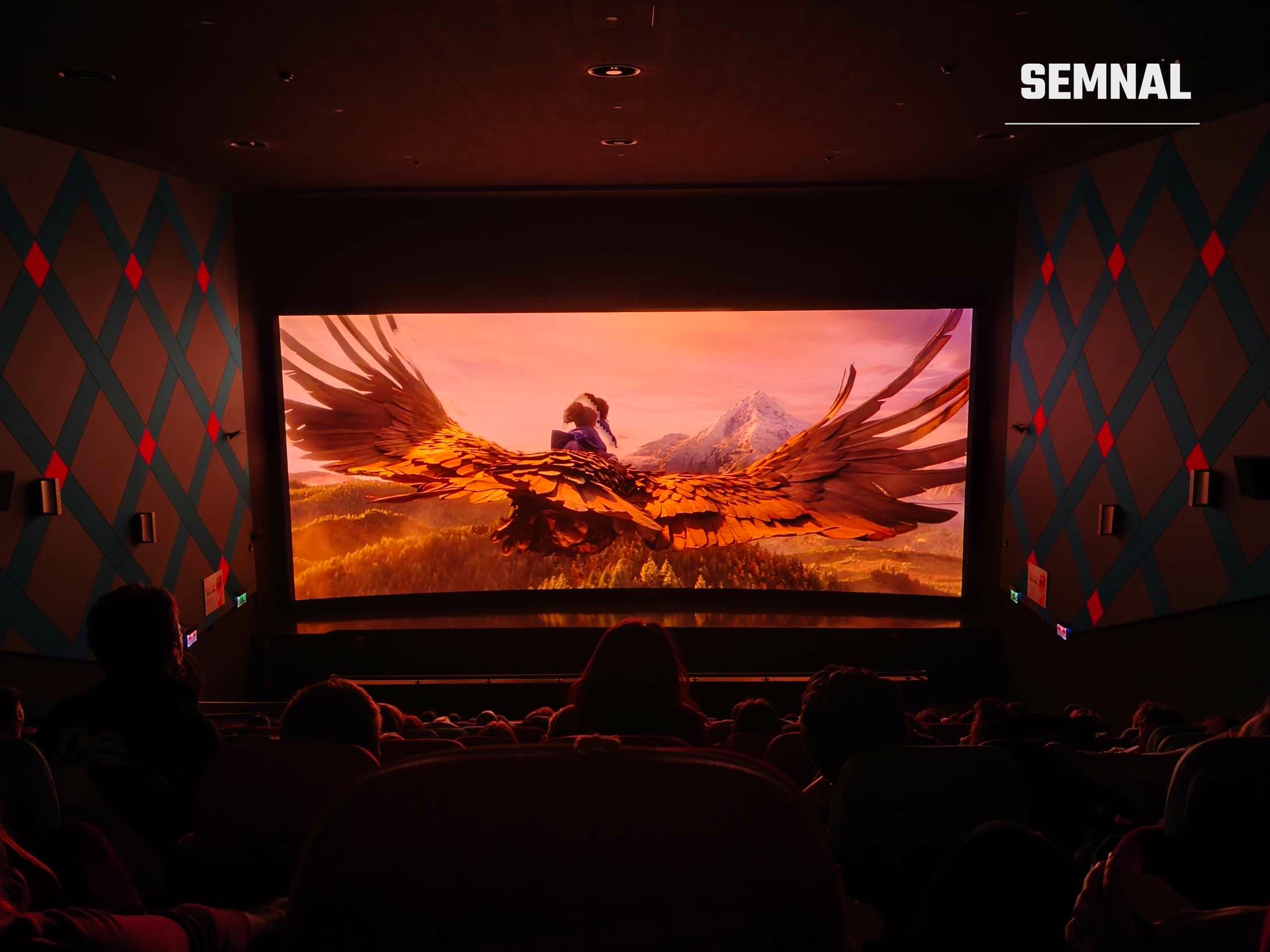 Sală de cinema întunecată în timpul proiecției Wildwood, cu o fată zburând pe un vultur uriaș deasupra unei păduri