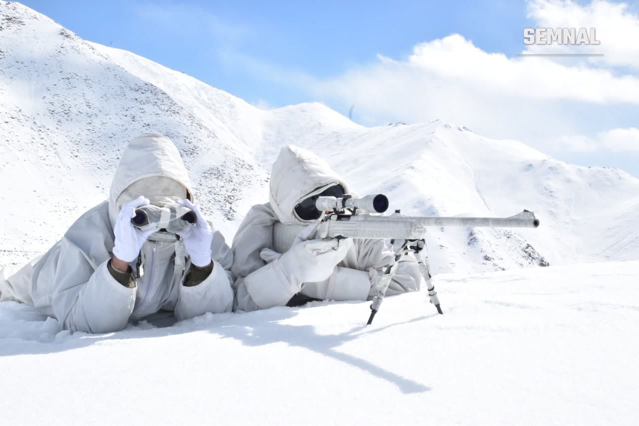 Doi militari ai Poliției de Frontieră Indo-Tibetane, în echipament alb de camuflaj, supraveghează zona cu binoclul și luneta pe un versant înzăpezit din Himalaya