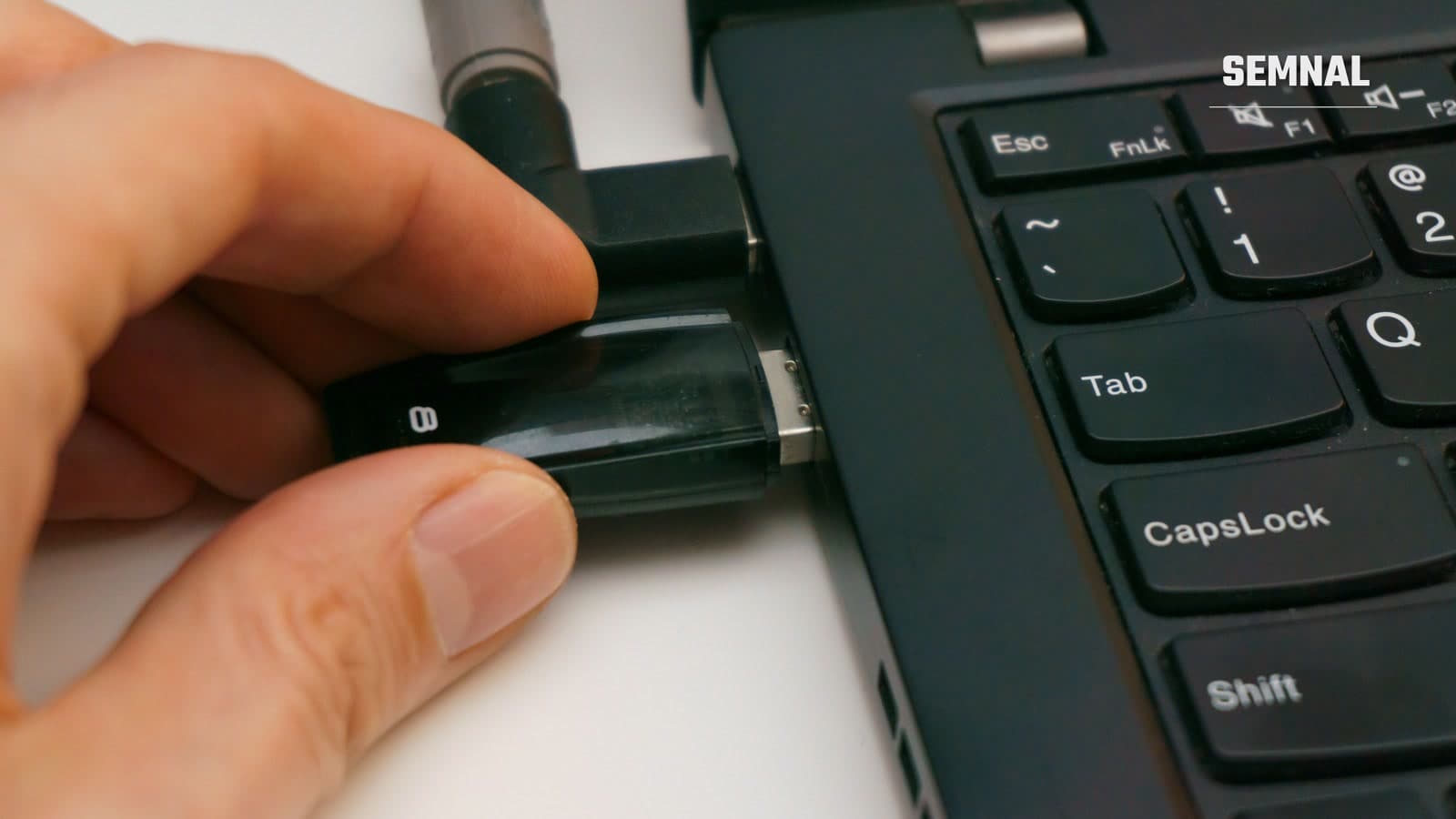 Mână care introduce un stick USB negru într-un port al unui laptop, cu tastatura laptopului vizibilă în dreapta
